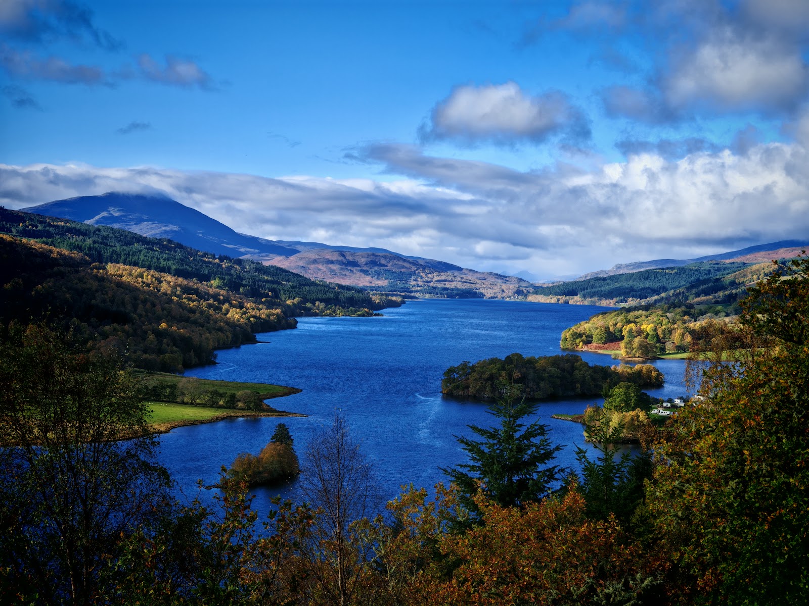 Loch Tummel and its islands from Queen's View, the hills beyond under a blue sky.
