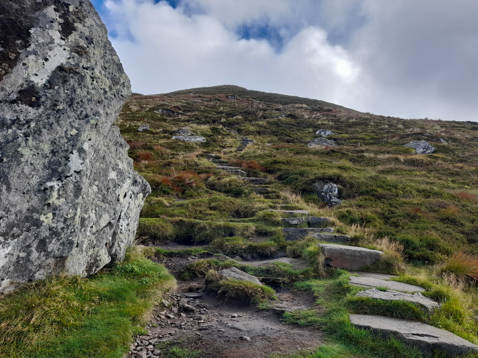 Stone-slab steps climb a grassy hillside path past a lichen-covered boulder