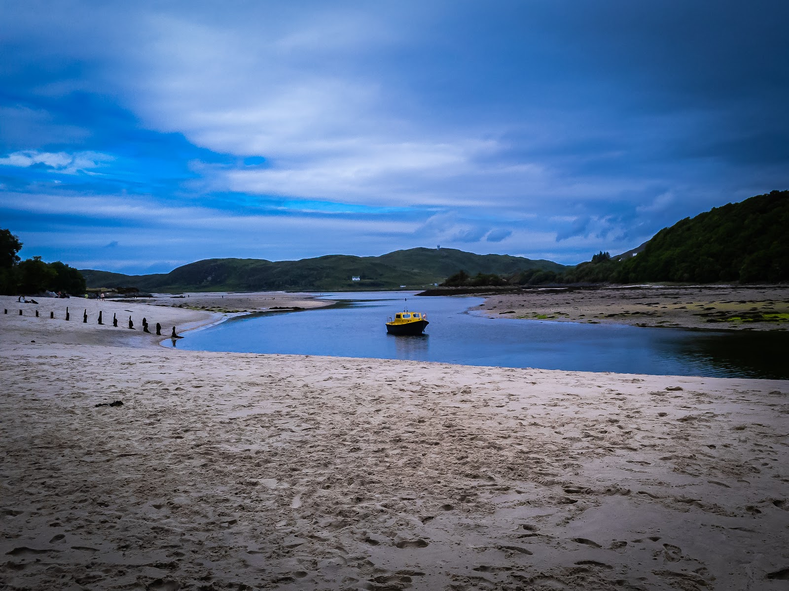 Yellow boat moored in a tidal river winding through a sandy beach