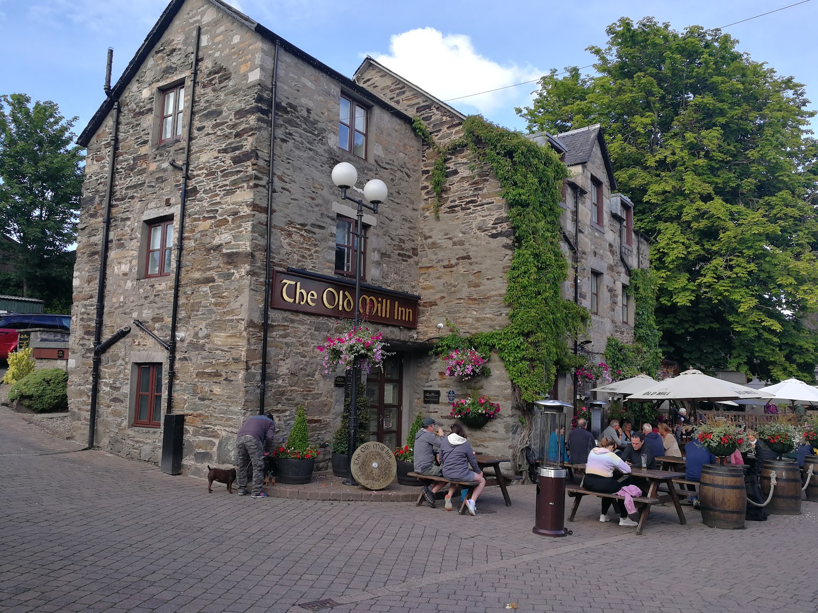 Stone building signed "The Old Mill Inn" with diners at outdoor picnic tables