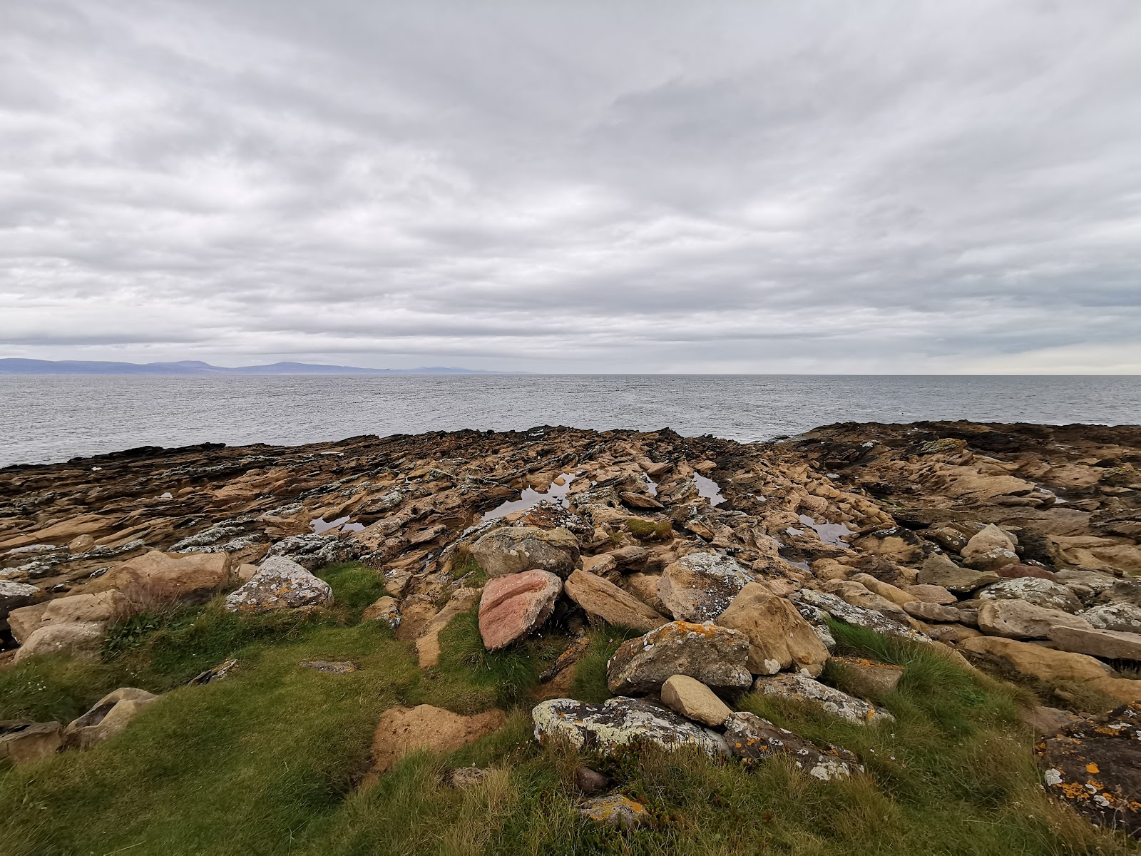 Flat rocky shoreline with lichen-covered stones facing distant hills across the water