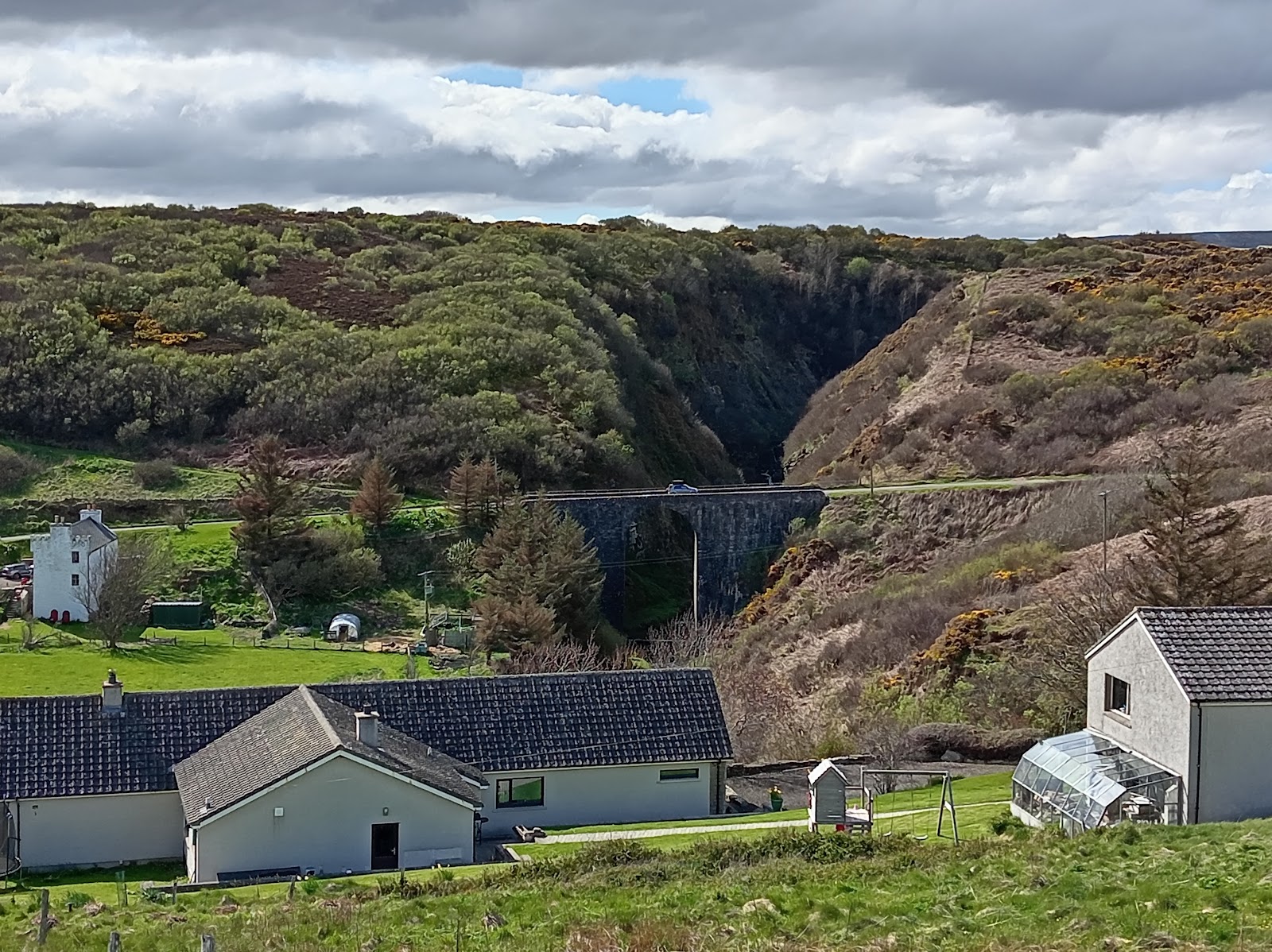 A stone bridge spans a wooded gorge above a village of bungalows