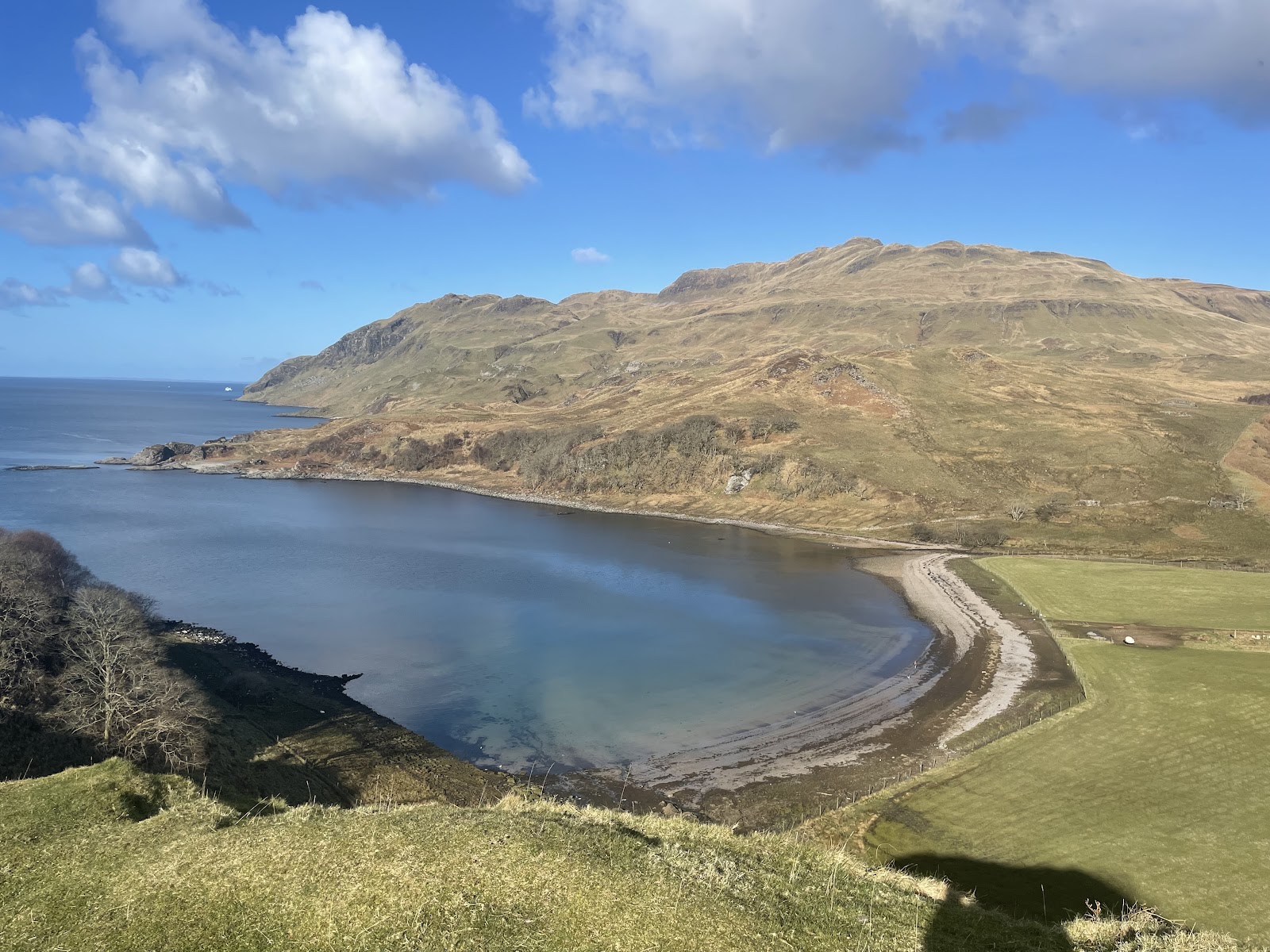 Camas nan Geall seen from above, a curving bay of calm water and a shingle spit below green slopes, Ben Hiant rising beyond.