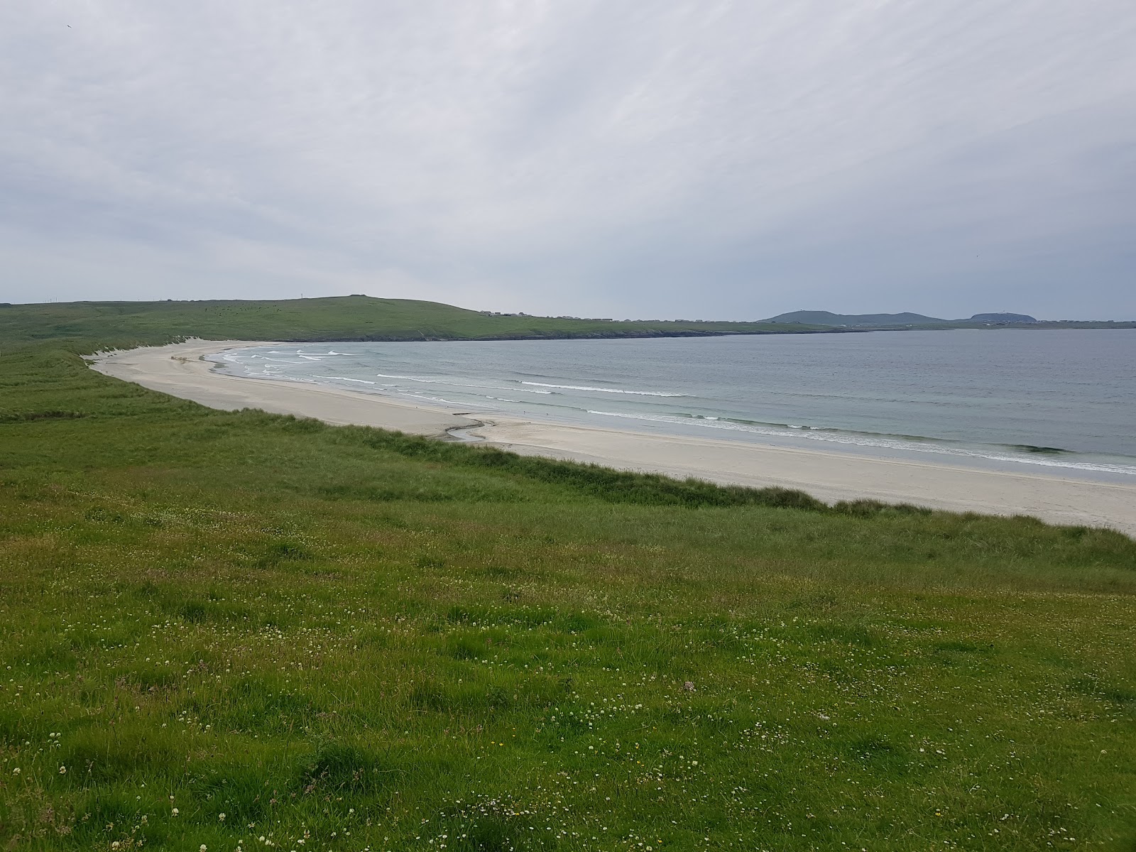 The sweep of sand round the Bay of Quendale beyond a green field.