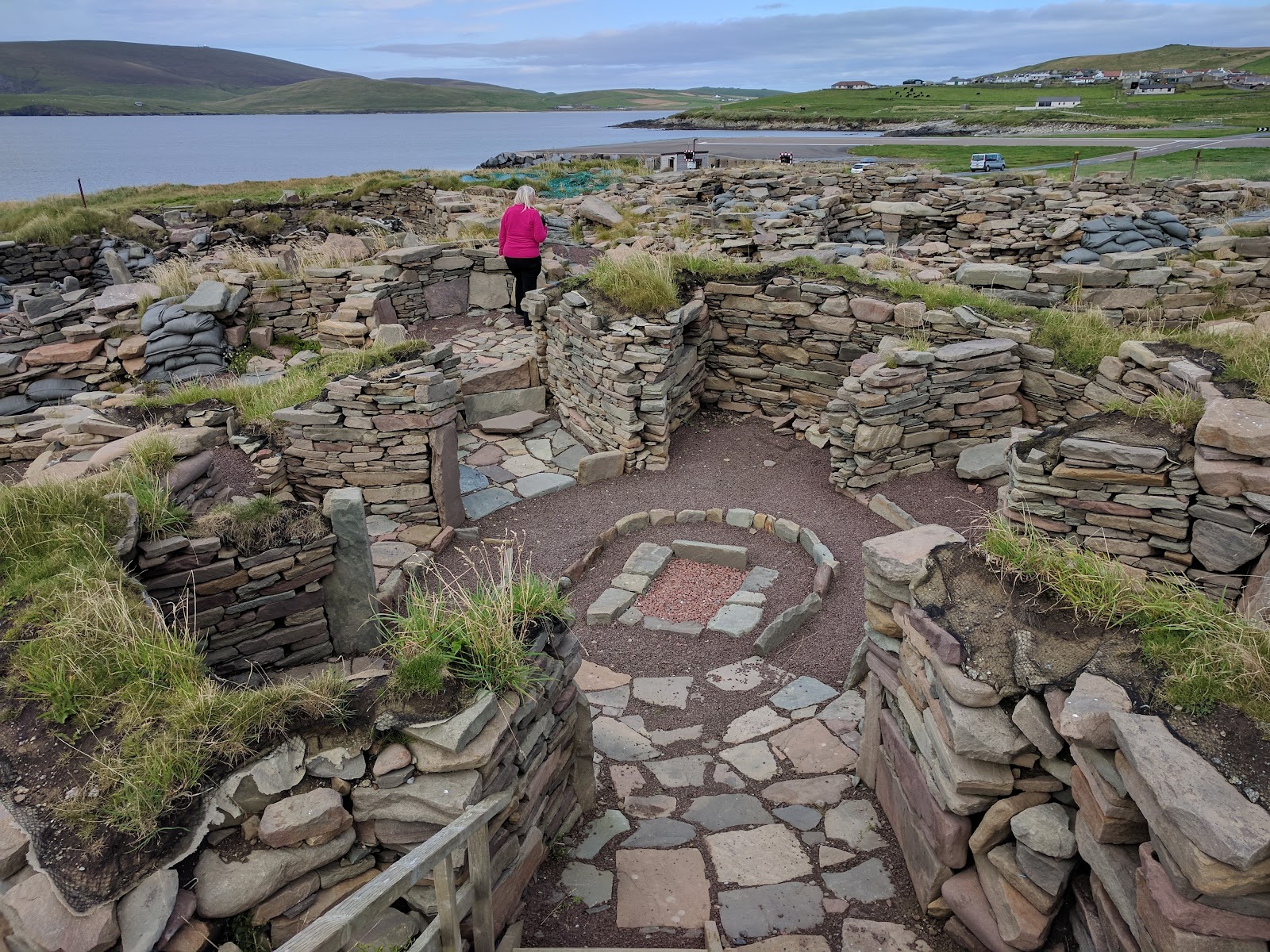 Visitor walks among stone walls and hearth of an Iron Age broch settlement
