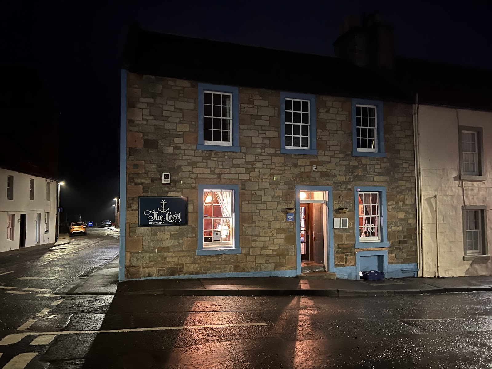 The Creel Restaurant lit up on a wet street corner at night
