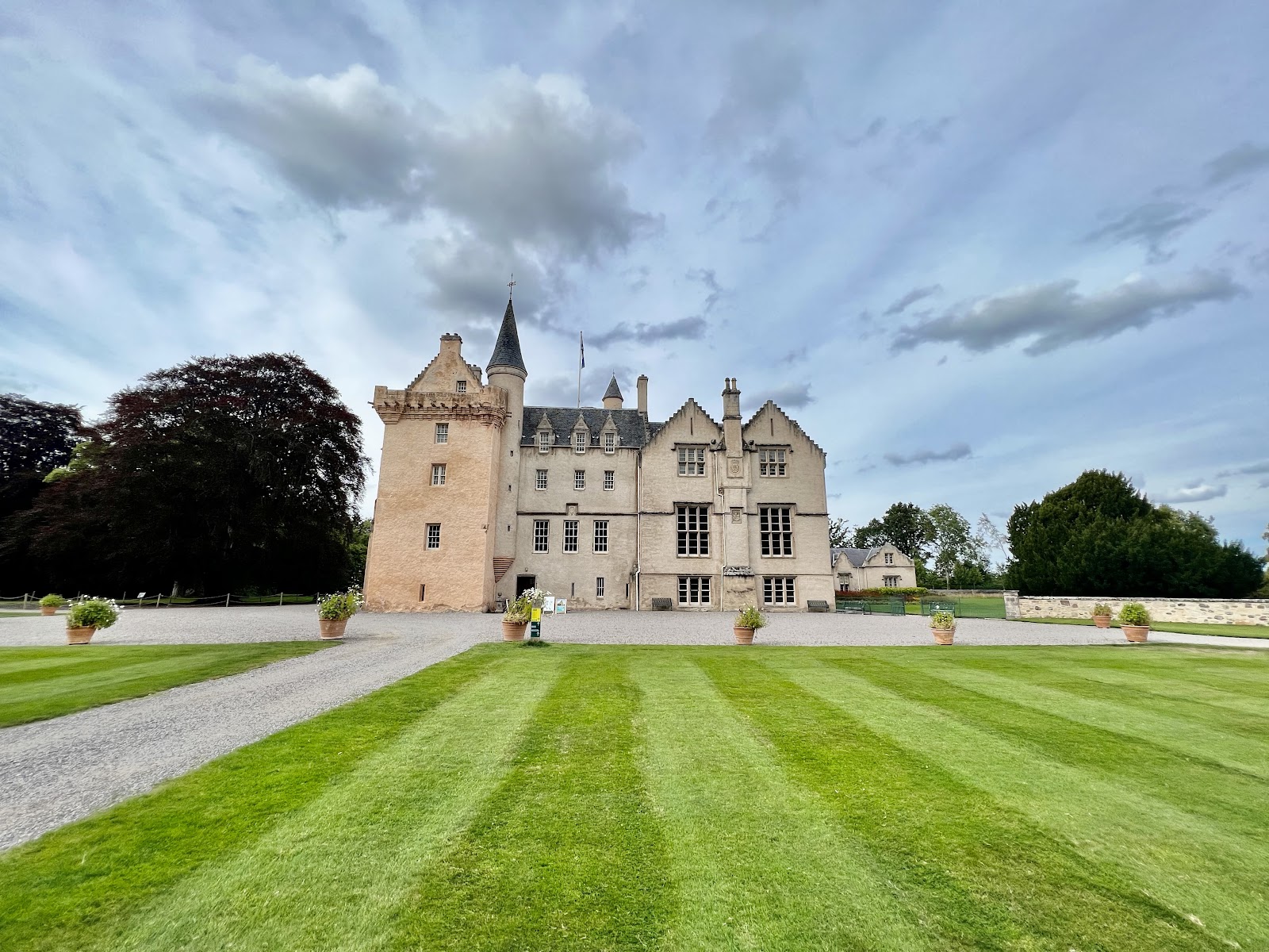 Turreted castle with crow-stepped gables overlooking a striped lawn and gravel drive