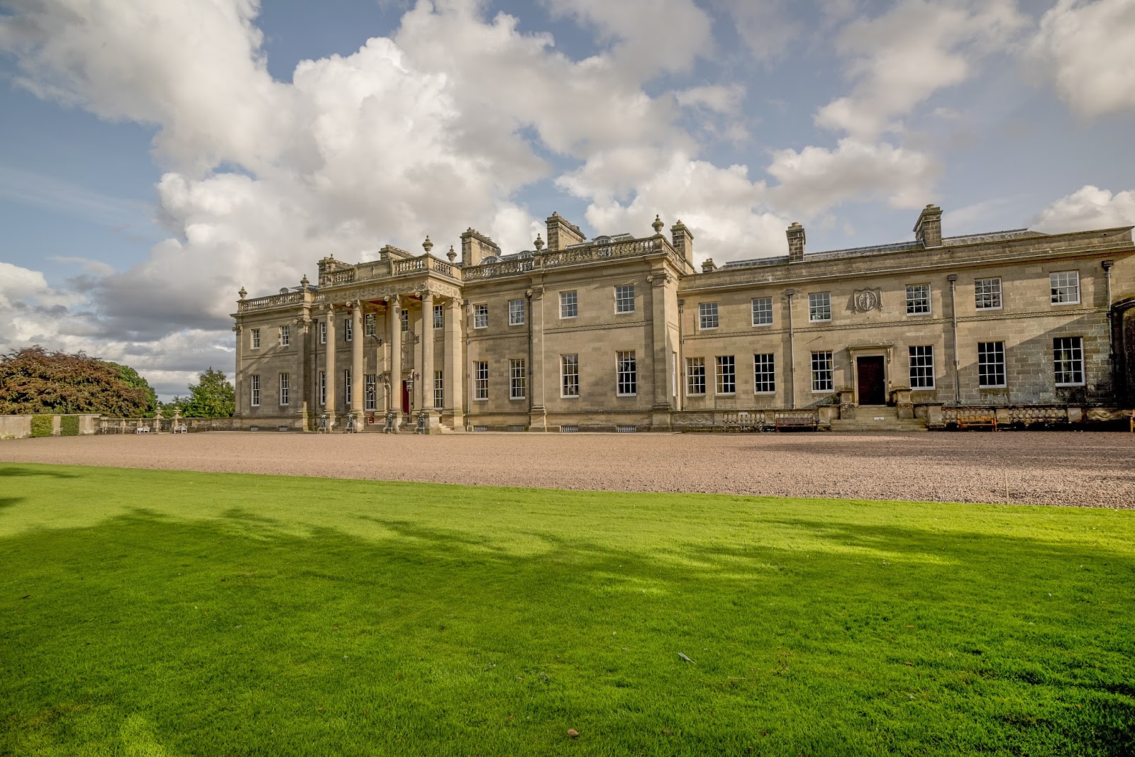 Long stone mansion with columned entrance, gravel drive and lawn stretching before it
