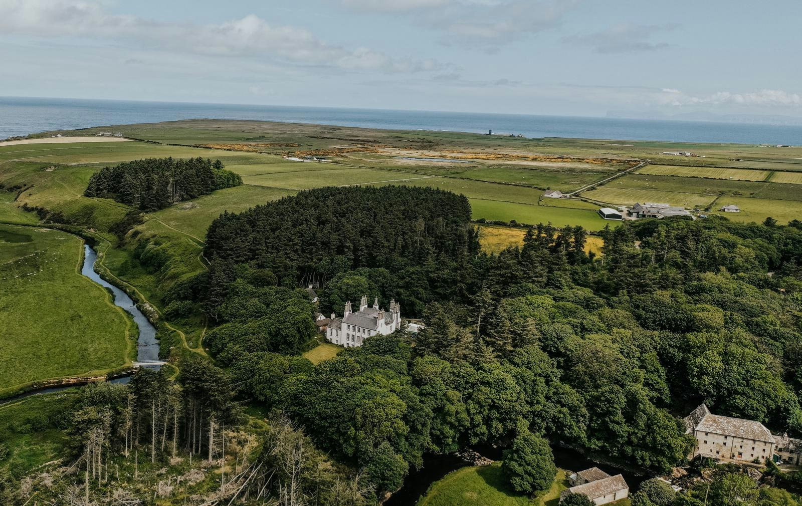 Forss House from the air, a white house among woods on a loop of the River Forss, fields and the sea beyond.