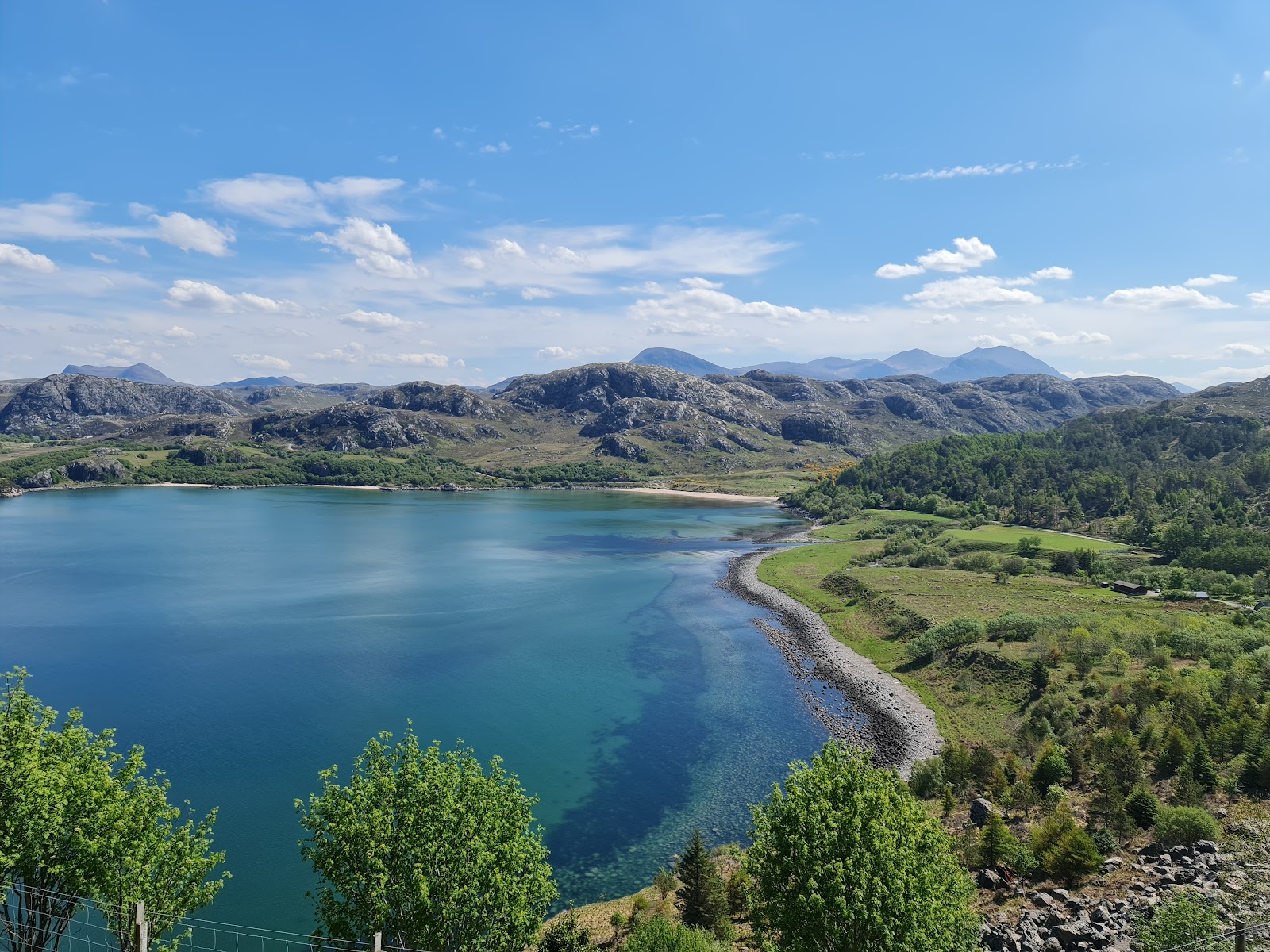 Turquoise sea loch curves between rocky hills and a pebbled shoreline