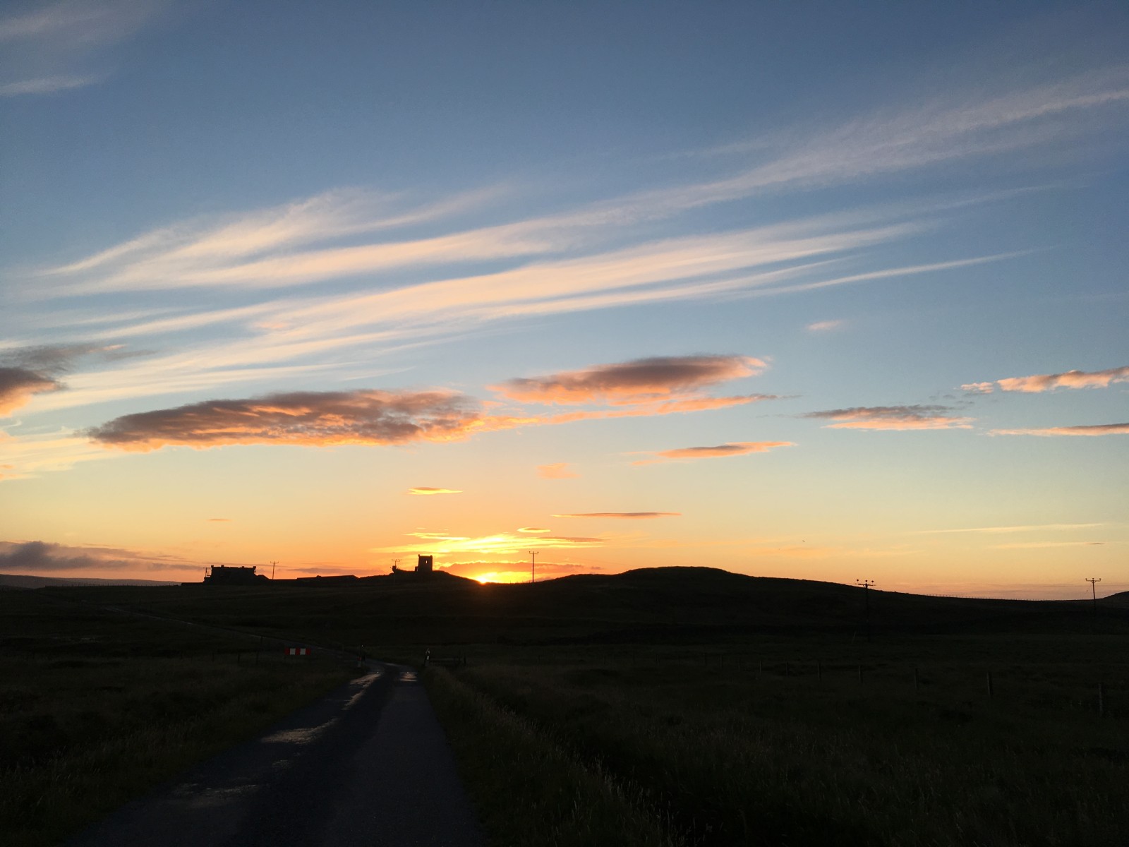 Dusk over the low hills of Fetlar, a road running towards a house on the skyline.