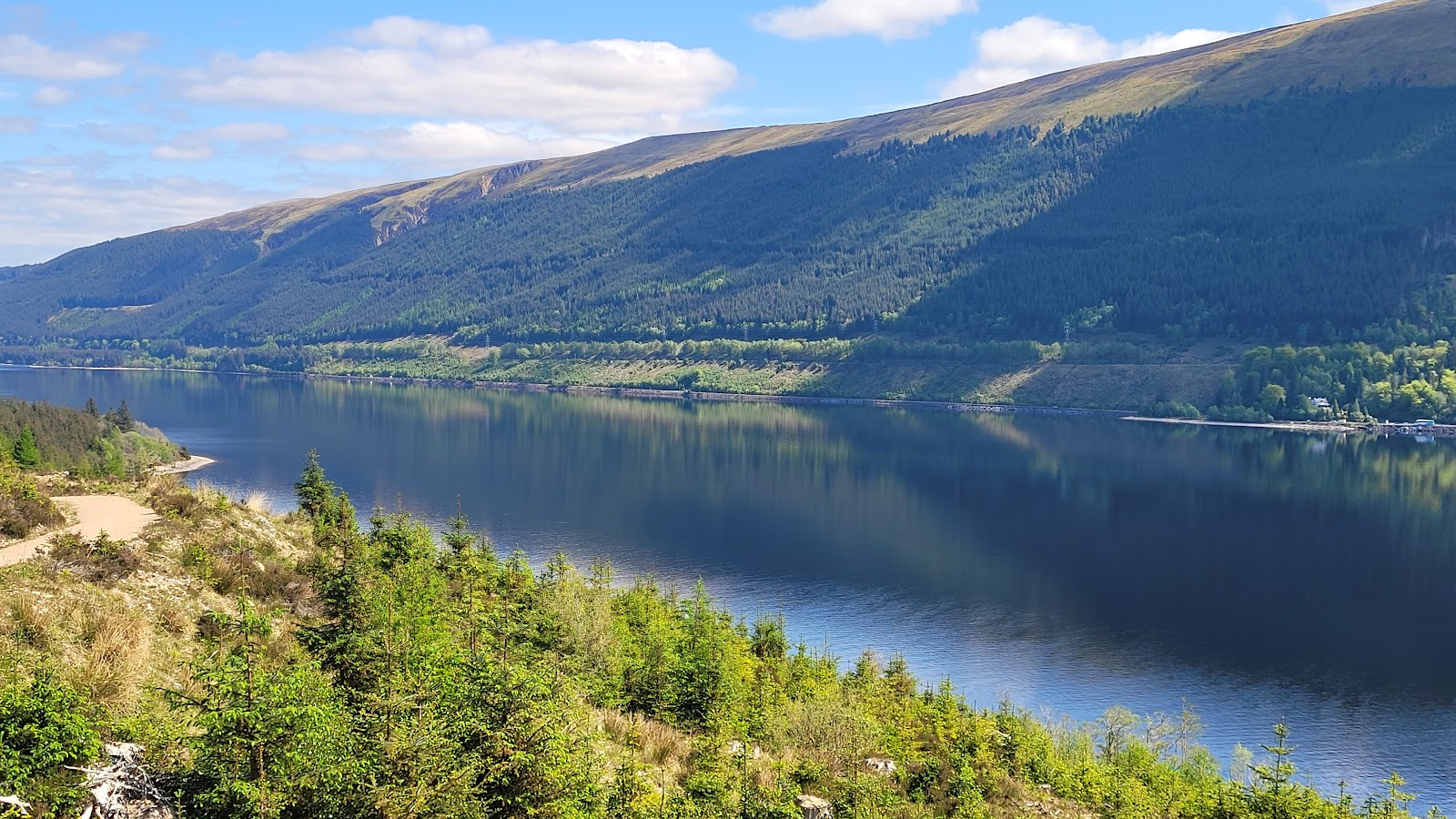 Loch Lochy from the Great Glen Way, the long calm loch below a forested hillside and a bare ridge.