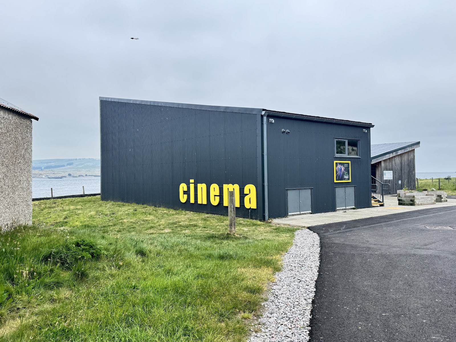 Yellow "cinema" lettering on a dark corrugated building beside the water