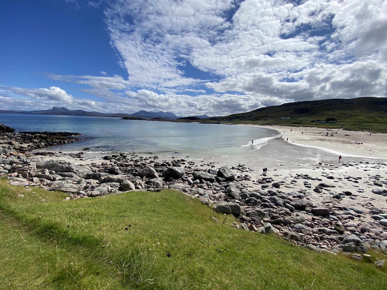 Mellon Udrigle's white sand and turquoise water beyond a rocky shore, low hills and distant peaks on the horizon.