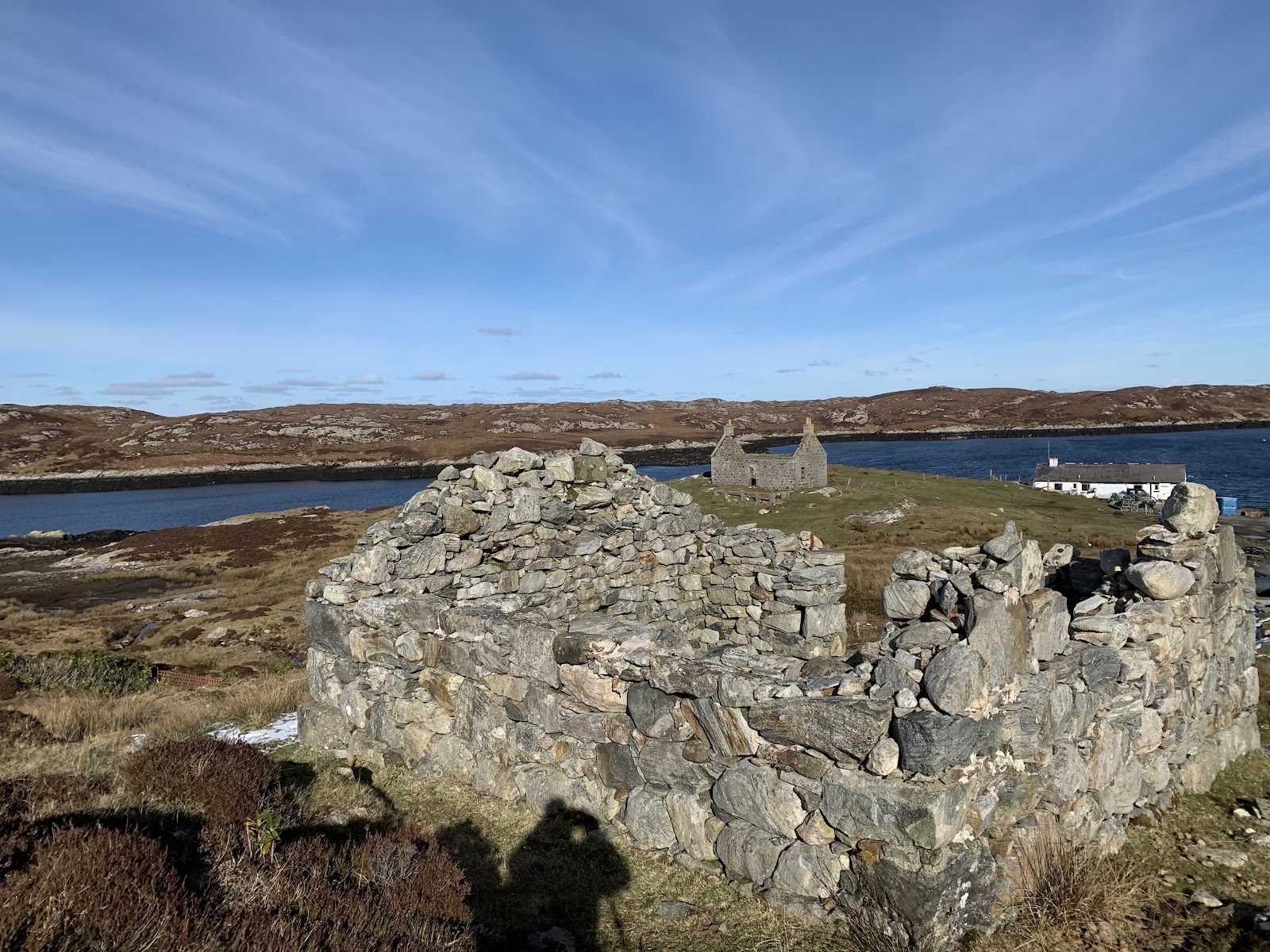 Ruined stone walls overlook a small stone house by a sea loch
