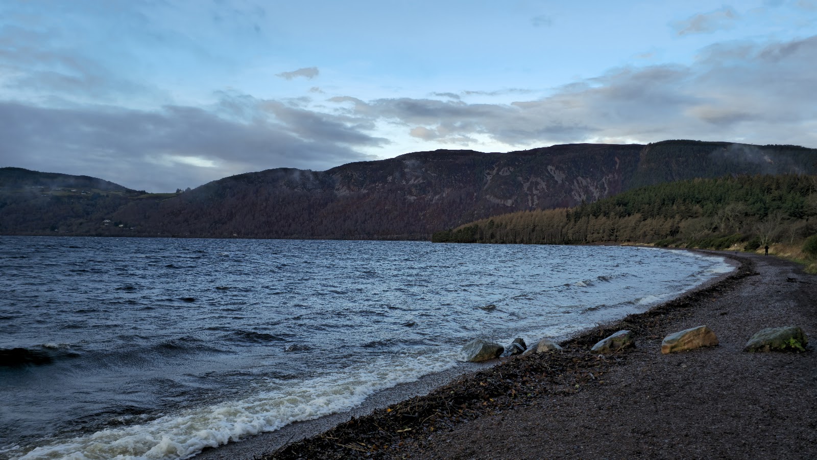 Waves breaking on the shingle of Dores Beach, Loch Ness running away between wooded hills.