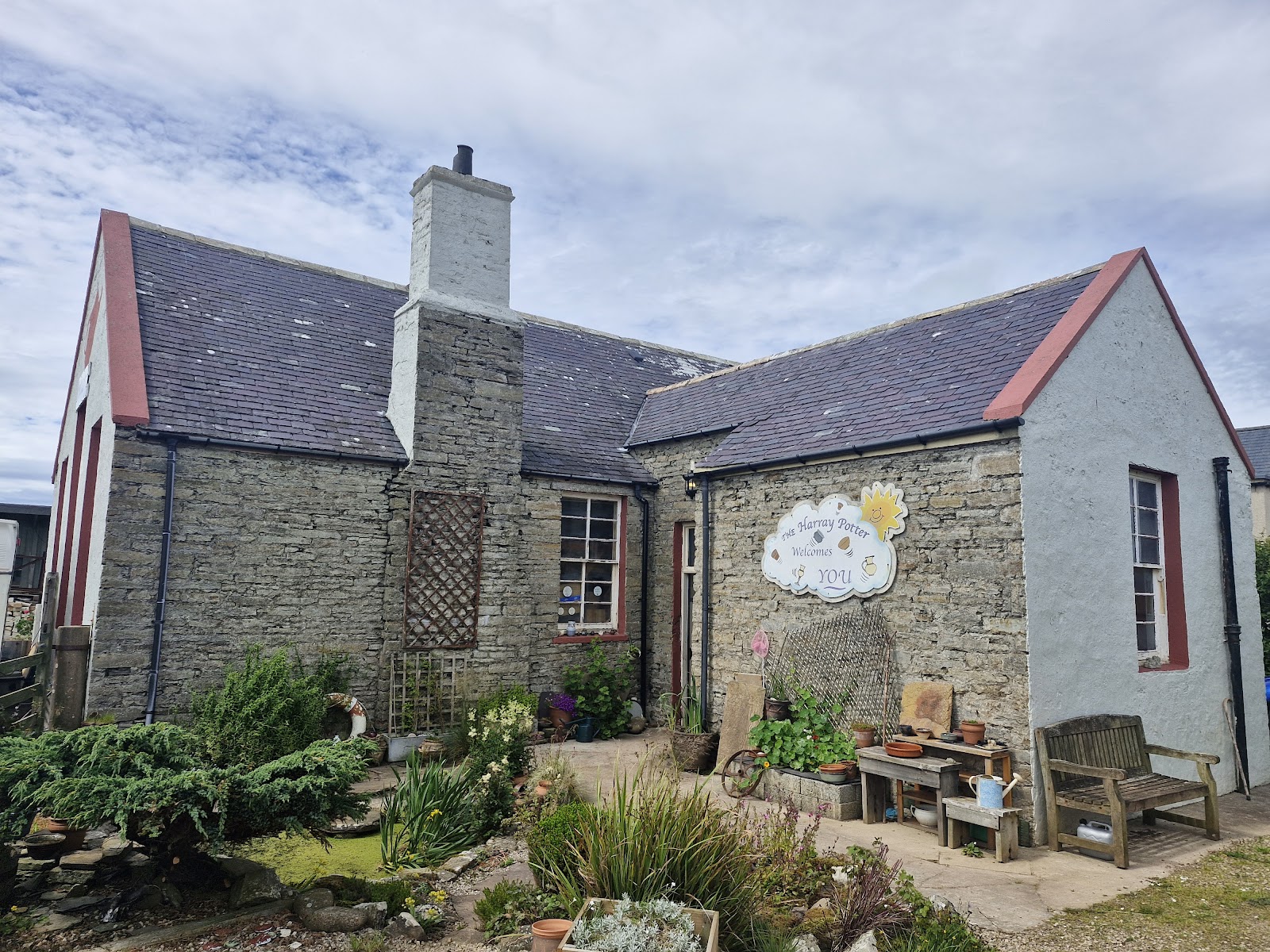 Fursbreck Pottery, a stone cottage with a red-edged roof and a garden of pots and benches, Harray.