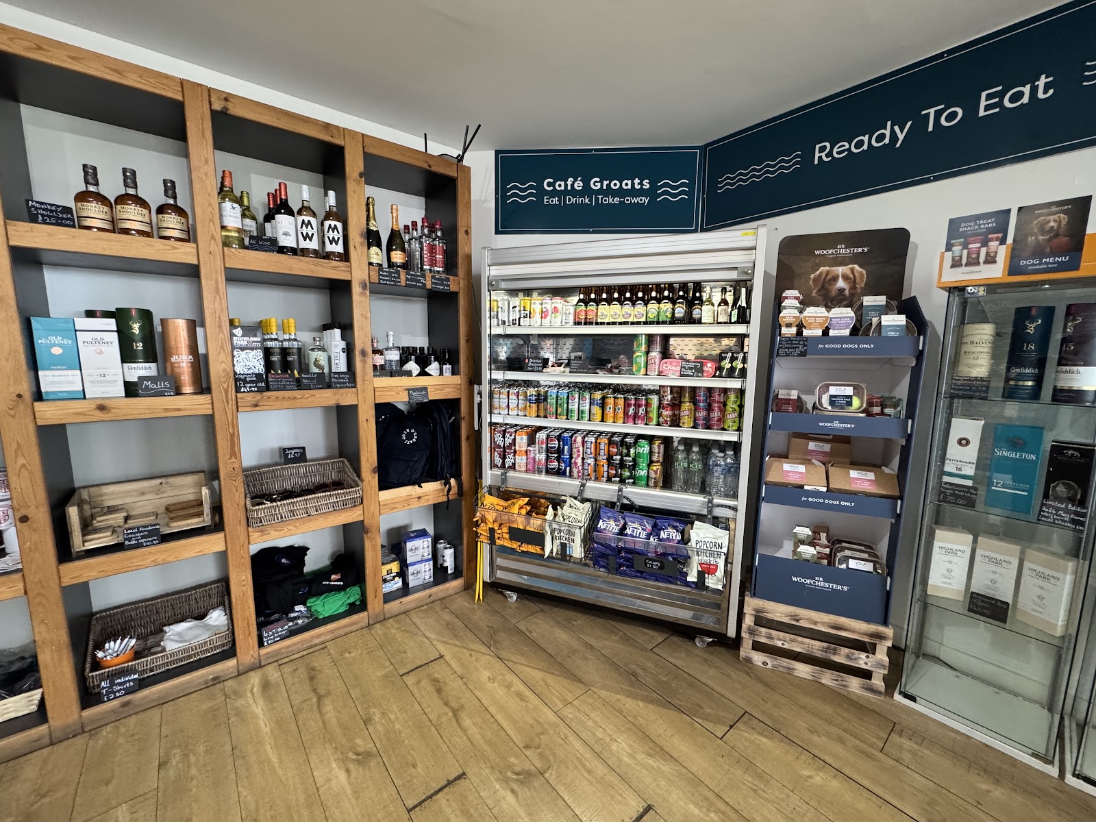 Whisky shelves and a fridge beside signs for Café Groats and Ready To Eat