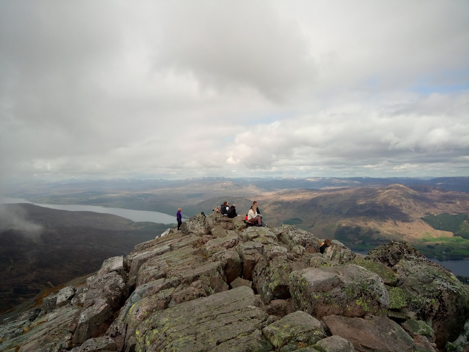 Walkers resting on the rocky summit of Schiehallion, lochs and hills far below.
