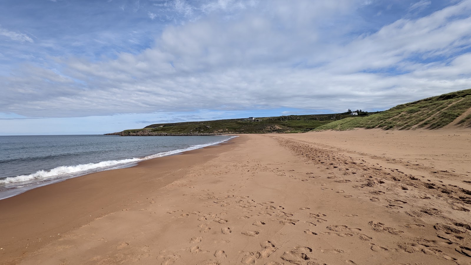 Footprints in the sand along a curving bay with grassy dunes and distant cottages