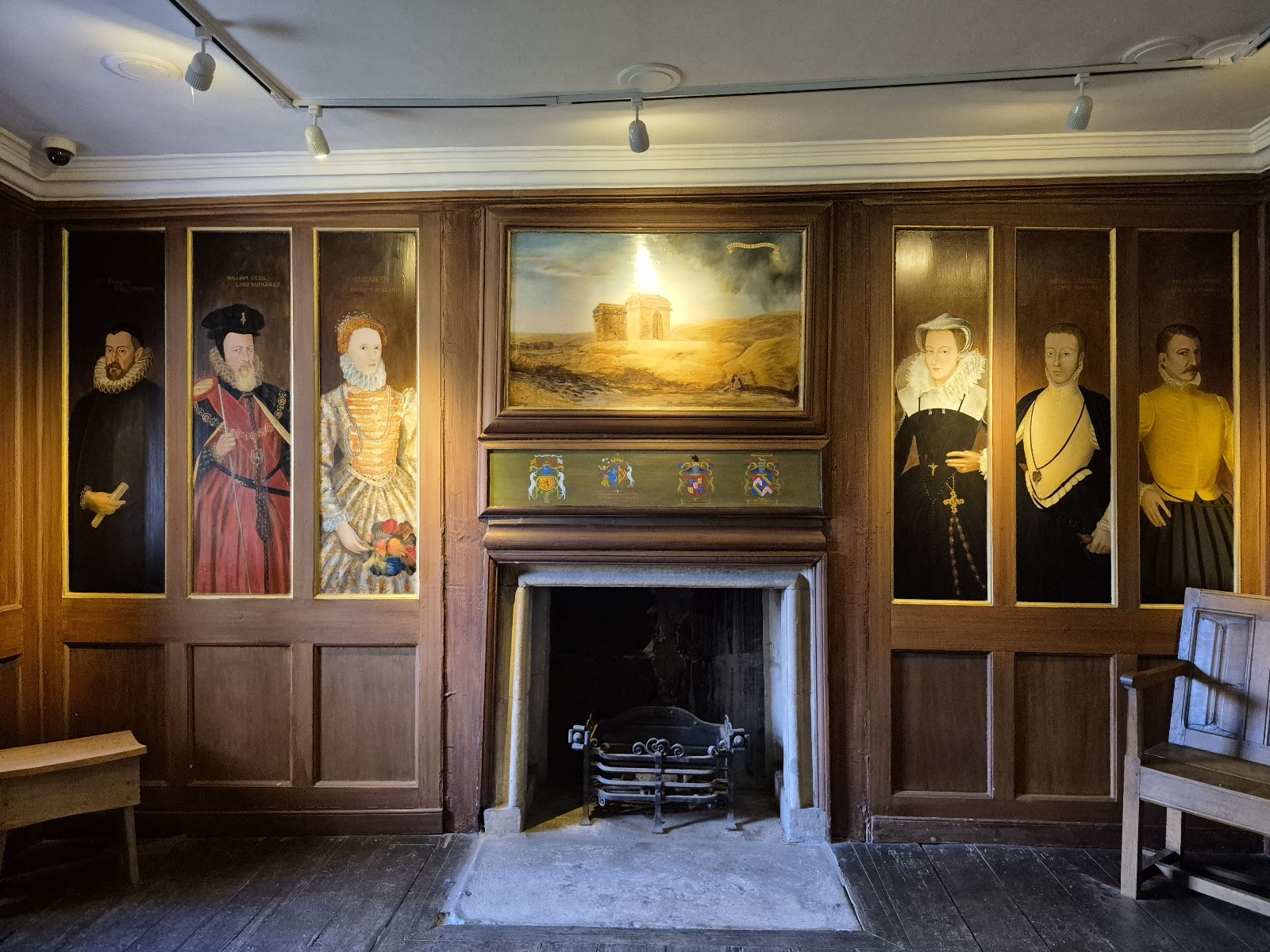 A panelled room in Mary Queen of Scots' House, Jedburgh, with a fireplace, a painting above it and portraits on the walls.