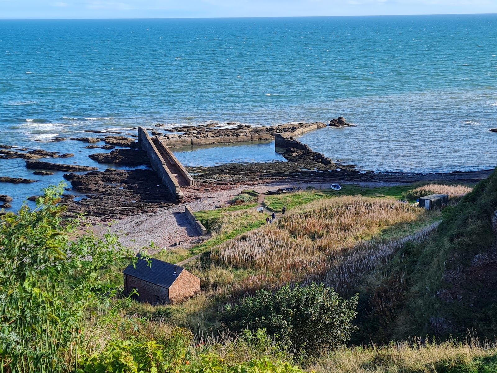 Ruined harbour walls enclose a rocky cove below a clifftop stone bothy