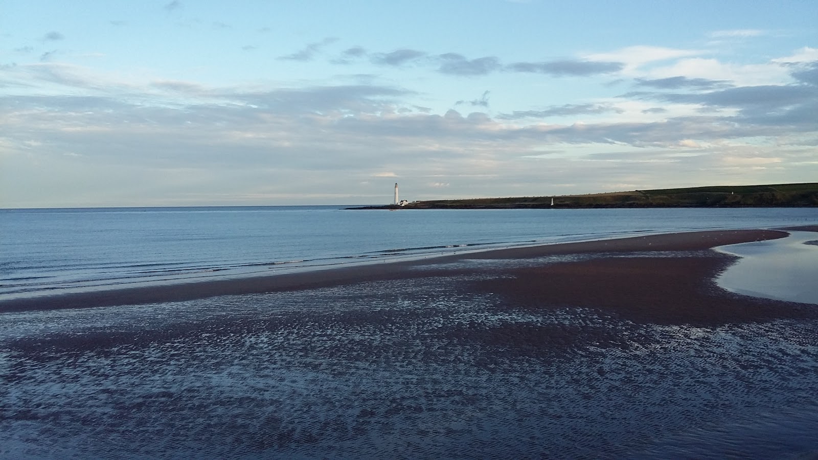 Wet sand stretches towards a distant lighthouse on the headland