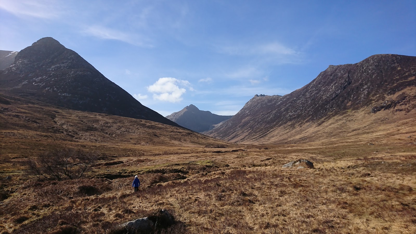 Walker crossing a wide glen towards distant jagged peaks