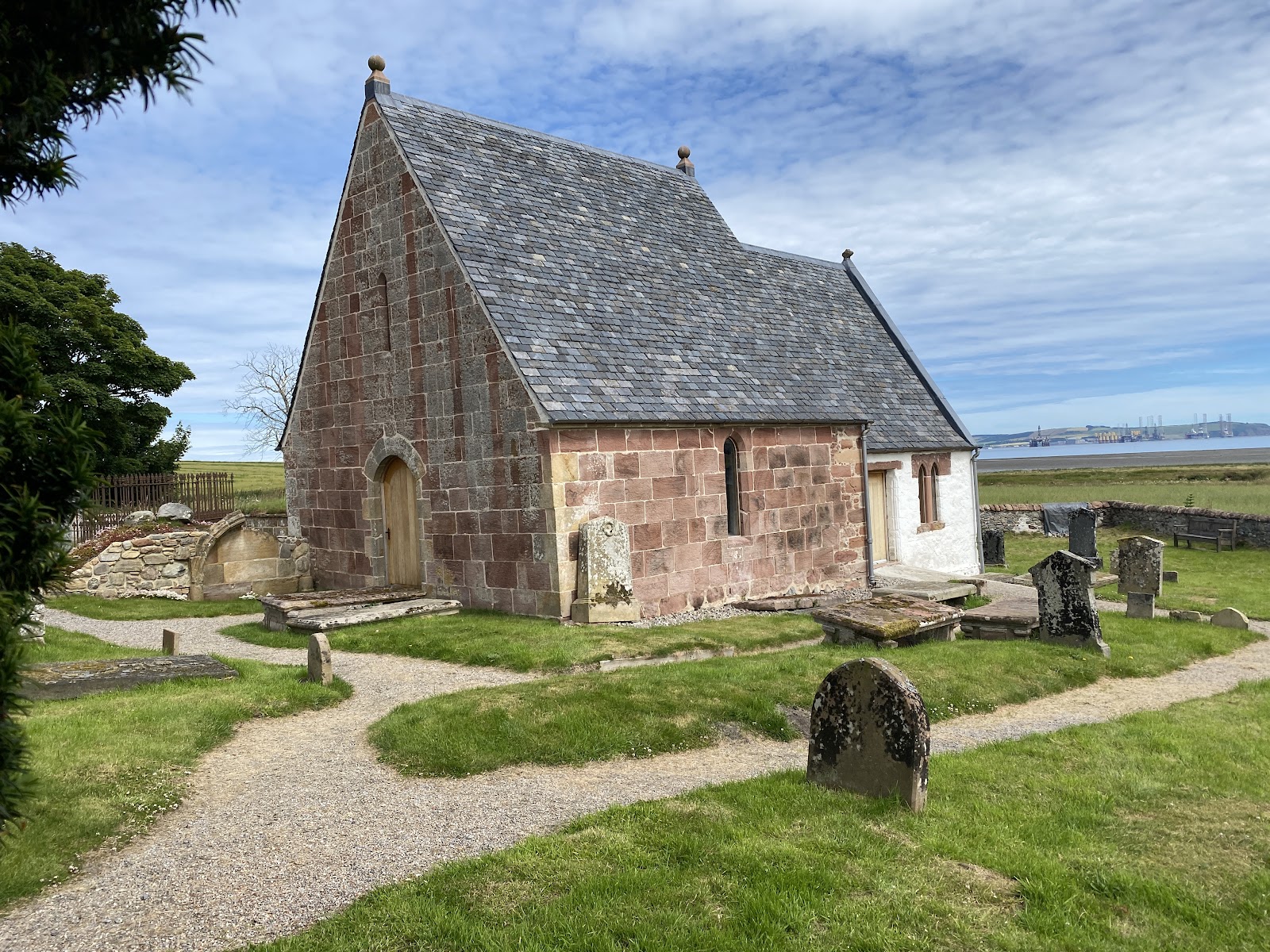 Kirkmichael's restored red sandstone church among old gravestones, a gravel path winding through the grass.
