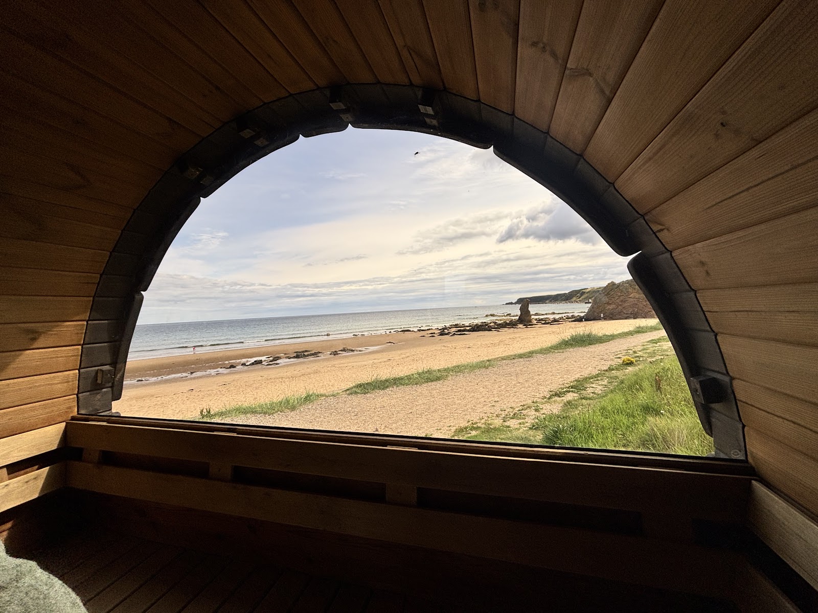 Sandy beach and sea seen through the arched window of a wooden sauna