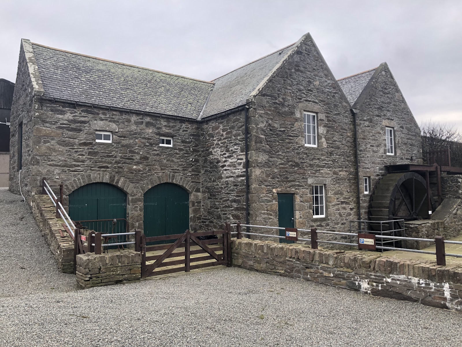 Quendale Mill's stone buildings and water wheel round a gravel yard.