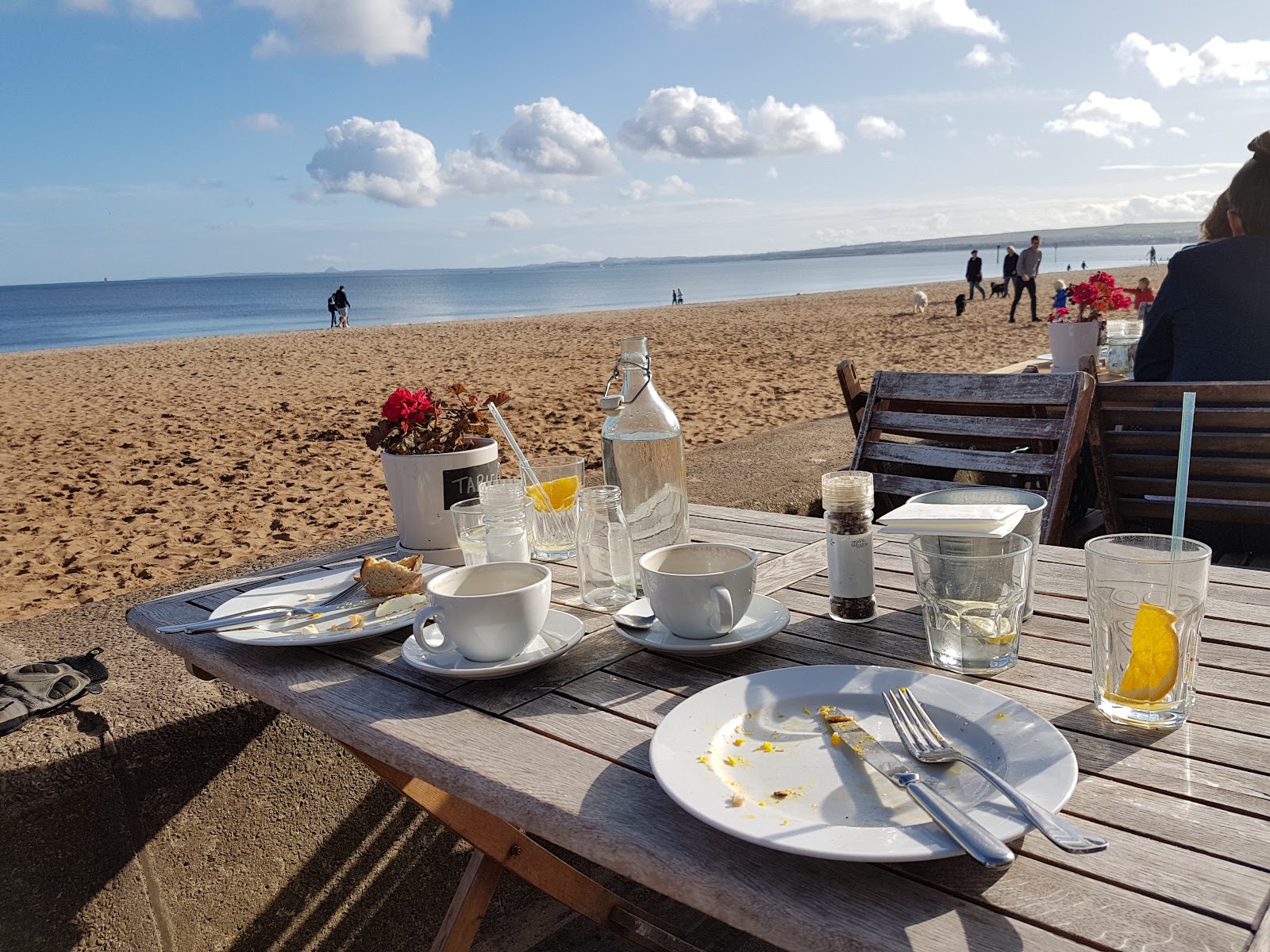 Empty plates and coffee cups on a wooden table overlooking a sandy beach