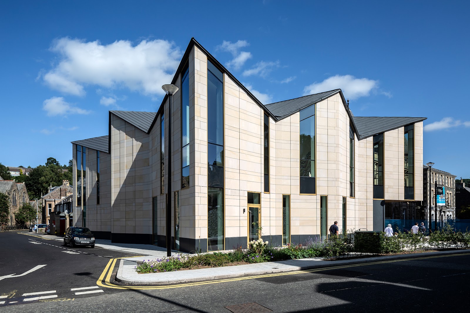 The Great Tapestry of Scotland's modern pale stone gallery with a zigzag roofline on a sunny street corner in Galashiels.