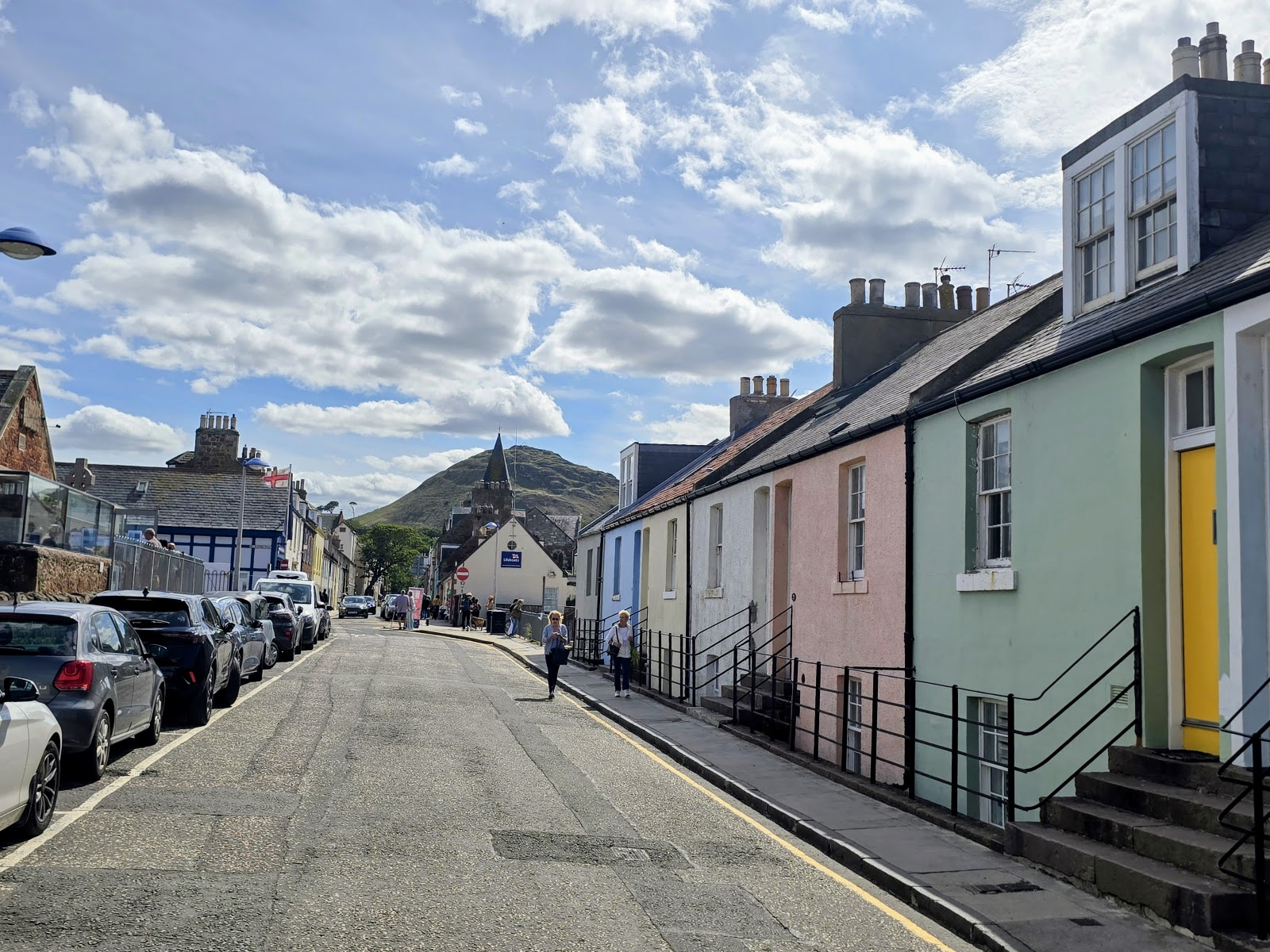 Pastel-coloured terraced houses line a sloping street beneath a hill