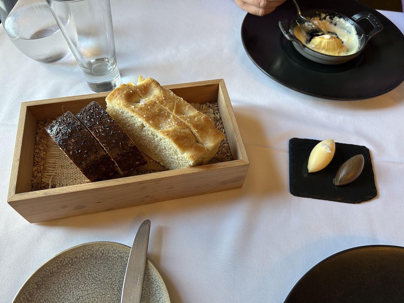 Sourdough and rye bread in a wooden box beside butter quenelles on slate
