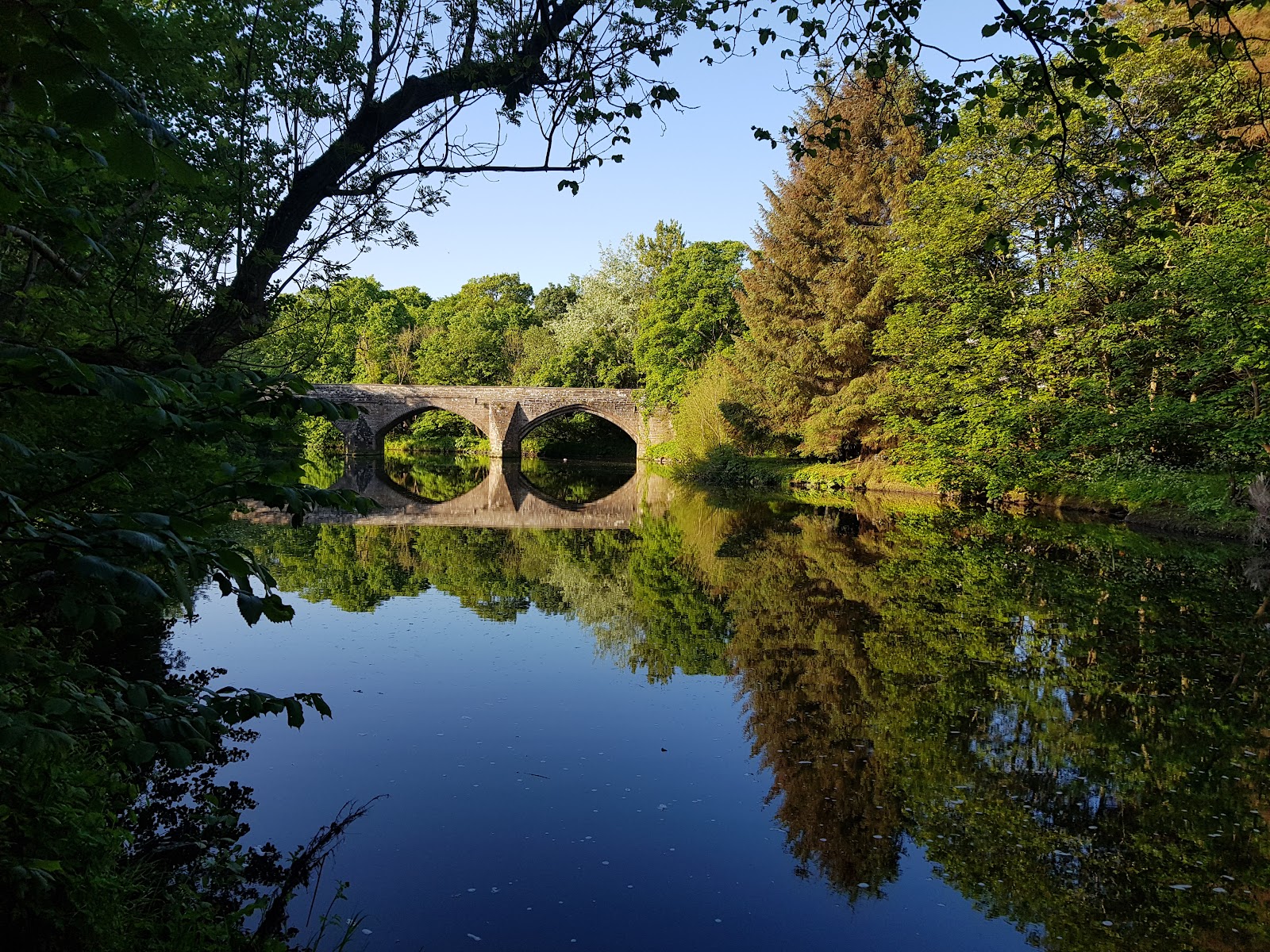 Cramond Brig reflected in the River Almond among trees.