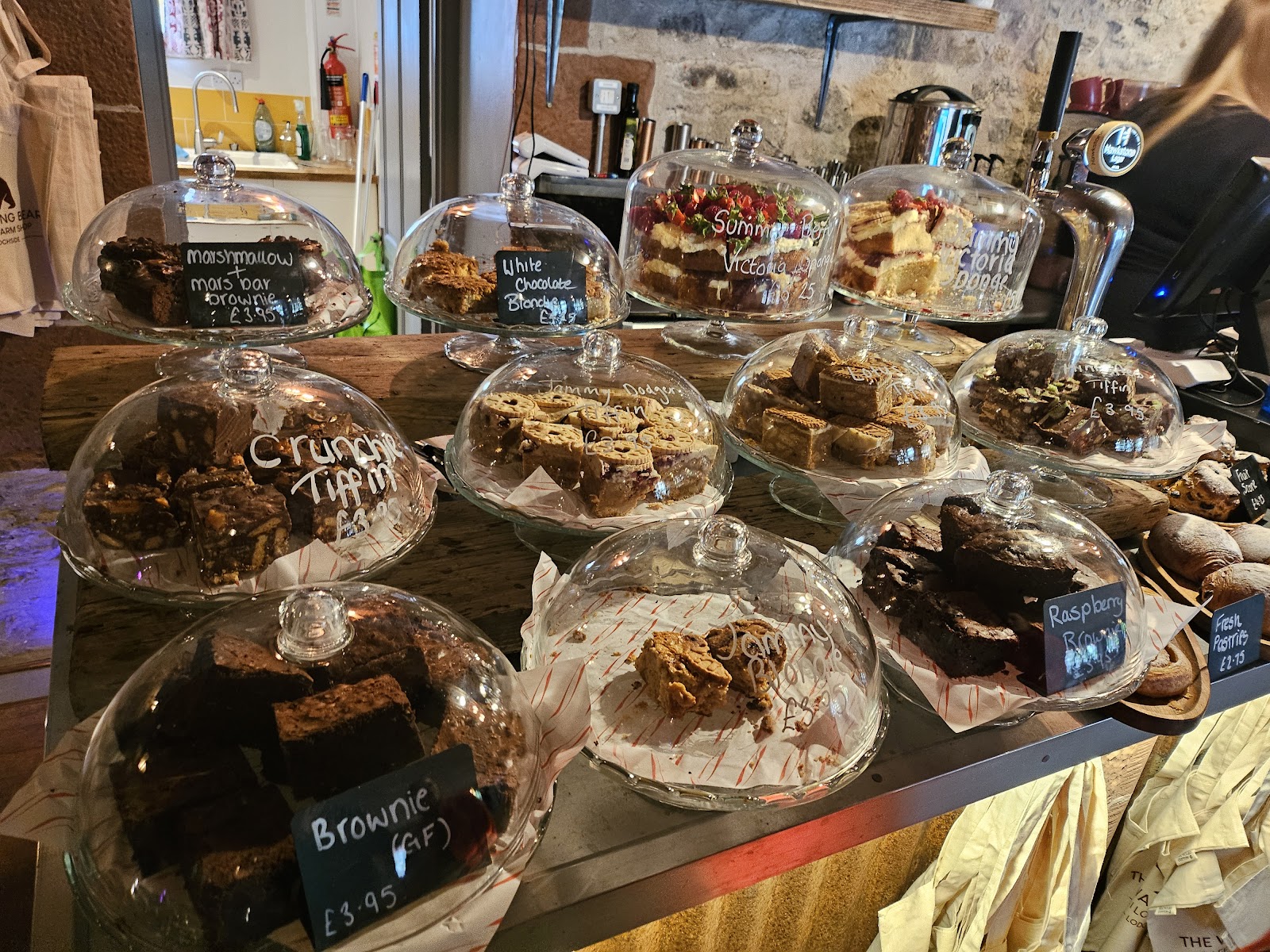 Glass cake stands display Crunchie Tiffin, Raspberry Brownie and Summer Berry Victoria Sponge on a farm shop counter