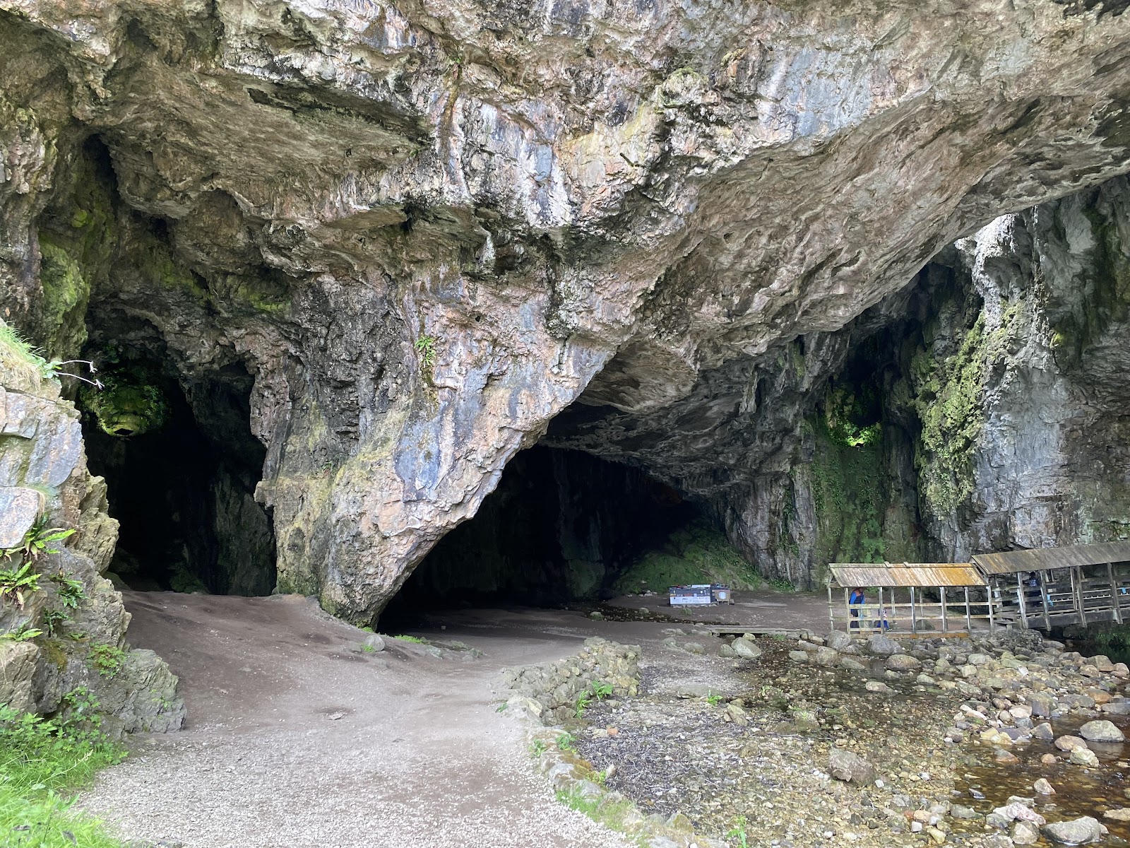 Vast limestone cave arch with a wooden viewing shelter beside the stream