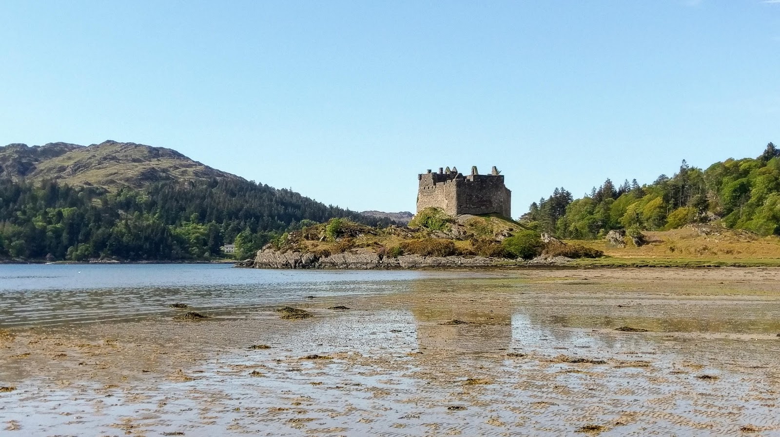 Ruined stone tower on a rocky headland above a tidal sandbank