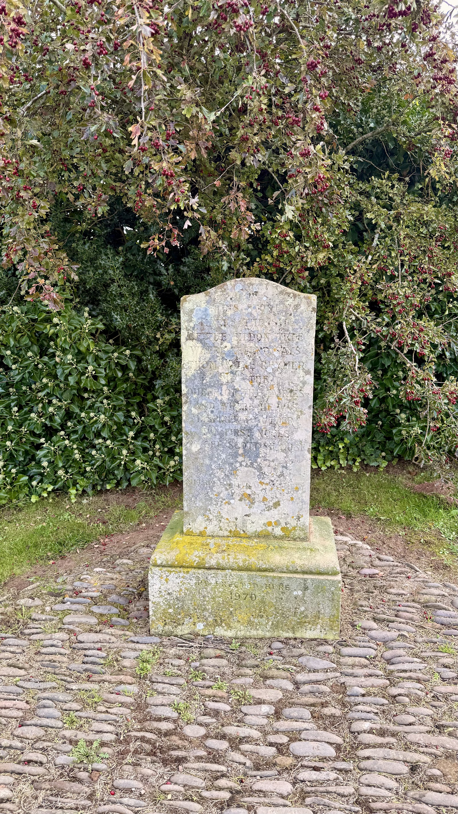 The Rhymer's Stone, a small upright memorial stone on a cobbled base in front of bushes.
