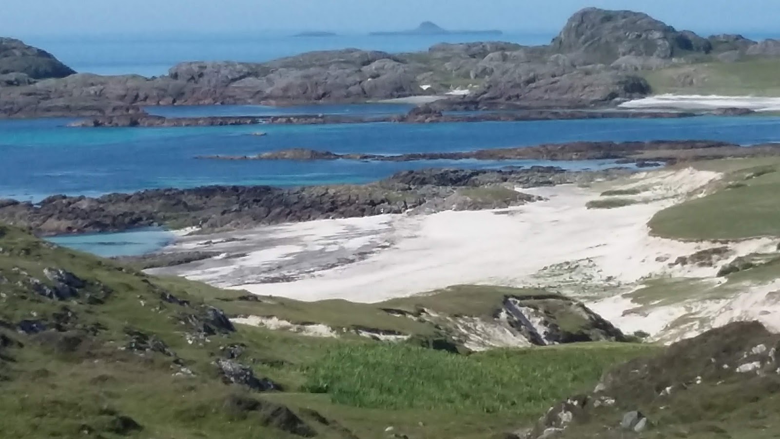 The white sand and blue water of the bay, rocks beyond.