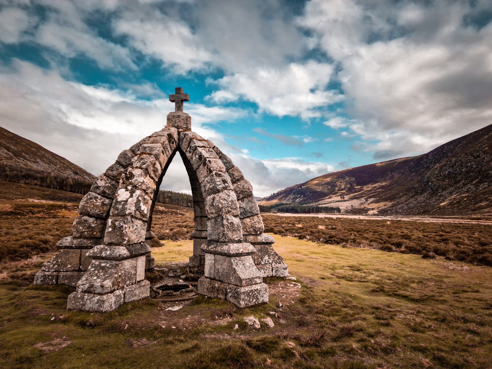 Stone arch topped with a cross stands alone in a glen