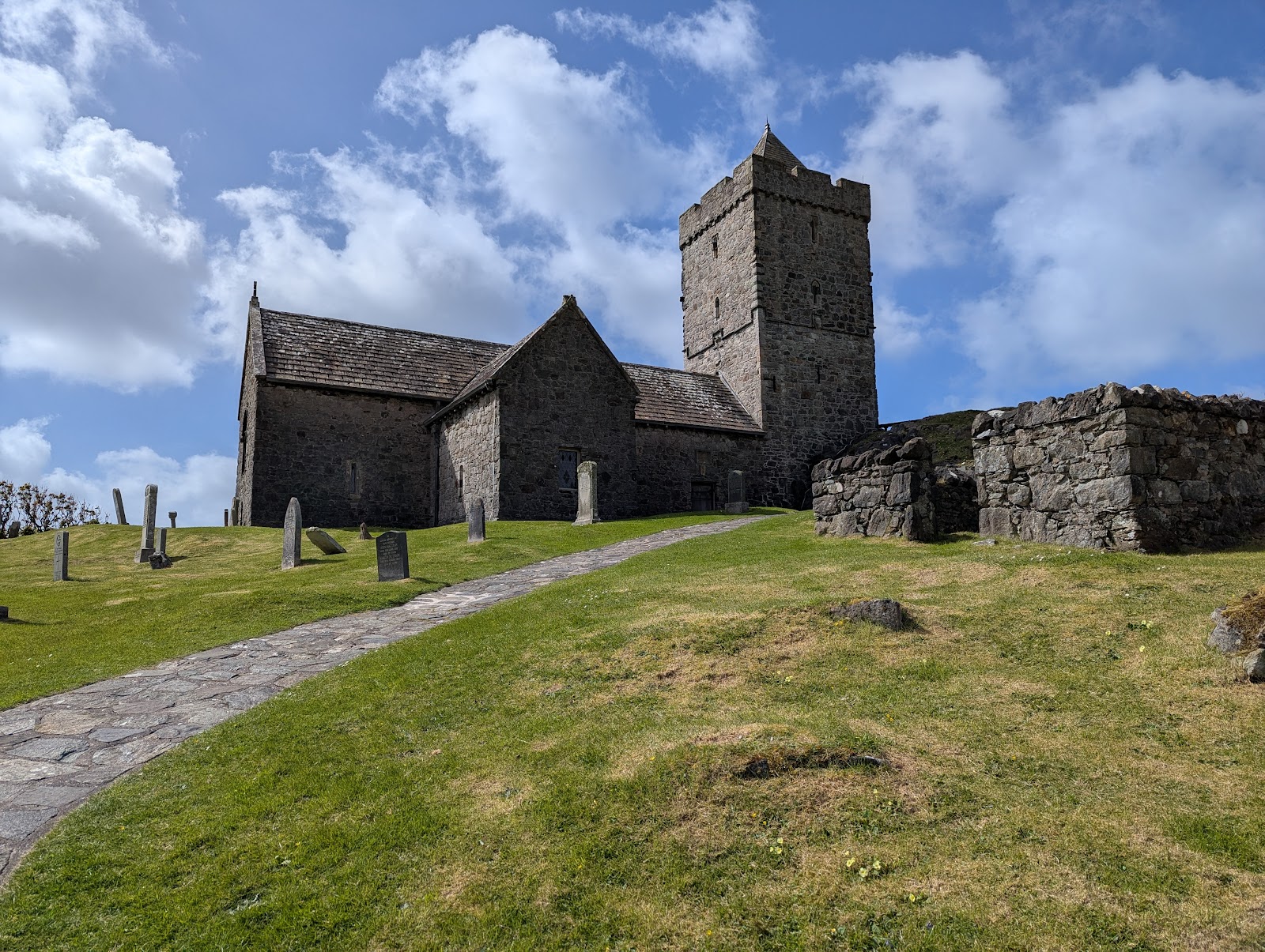 St Clement's Church at Rodel, its square tower rising above the churchyard under a blue sky.