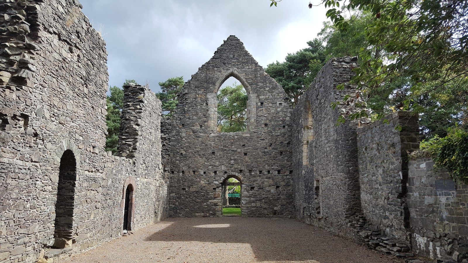 Roofless stone chapel ruin with a pointed arch window and gravel floor