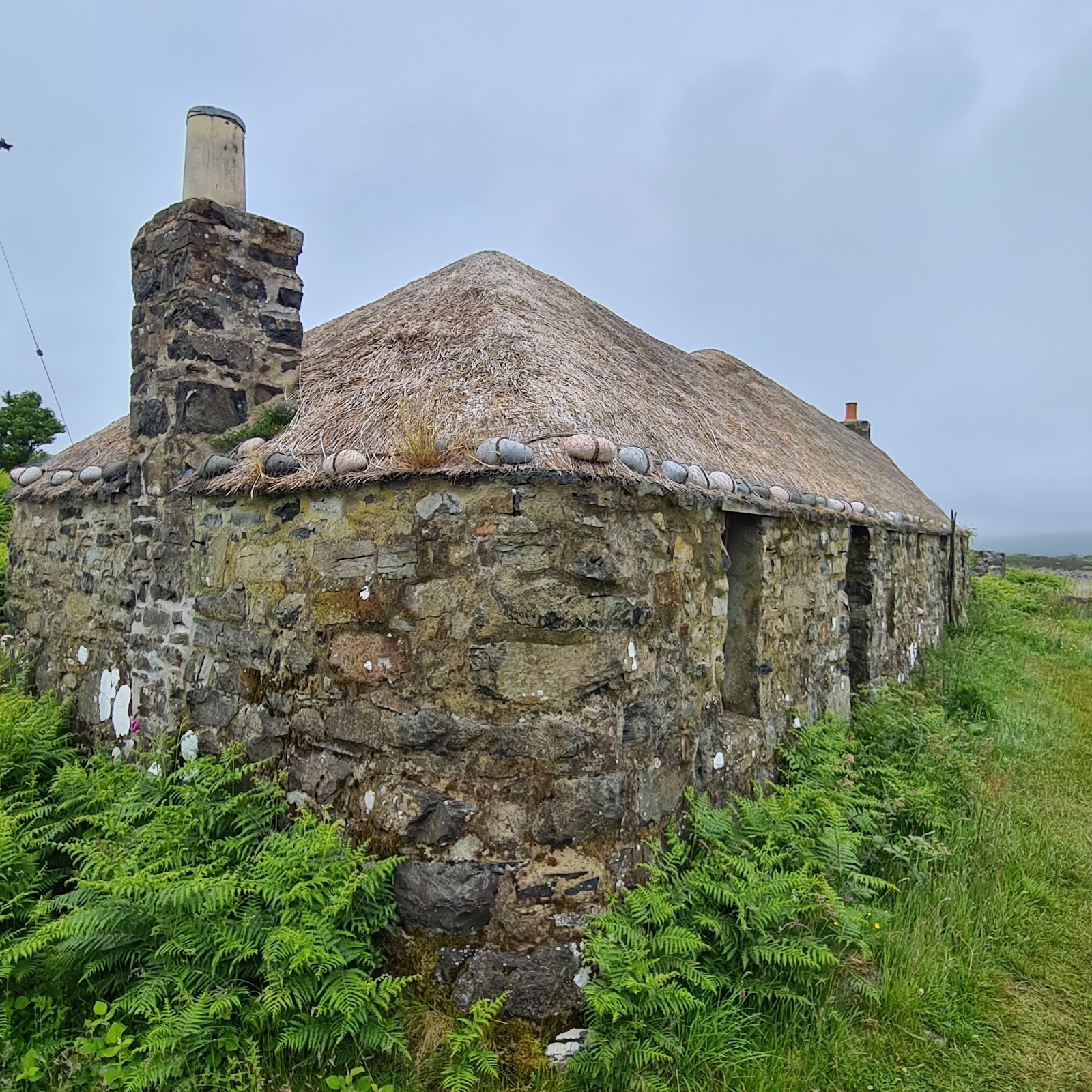 Sheila's Cottage on Ulva, a restored thatched croft house of stone among ferns.