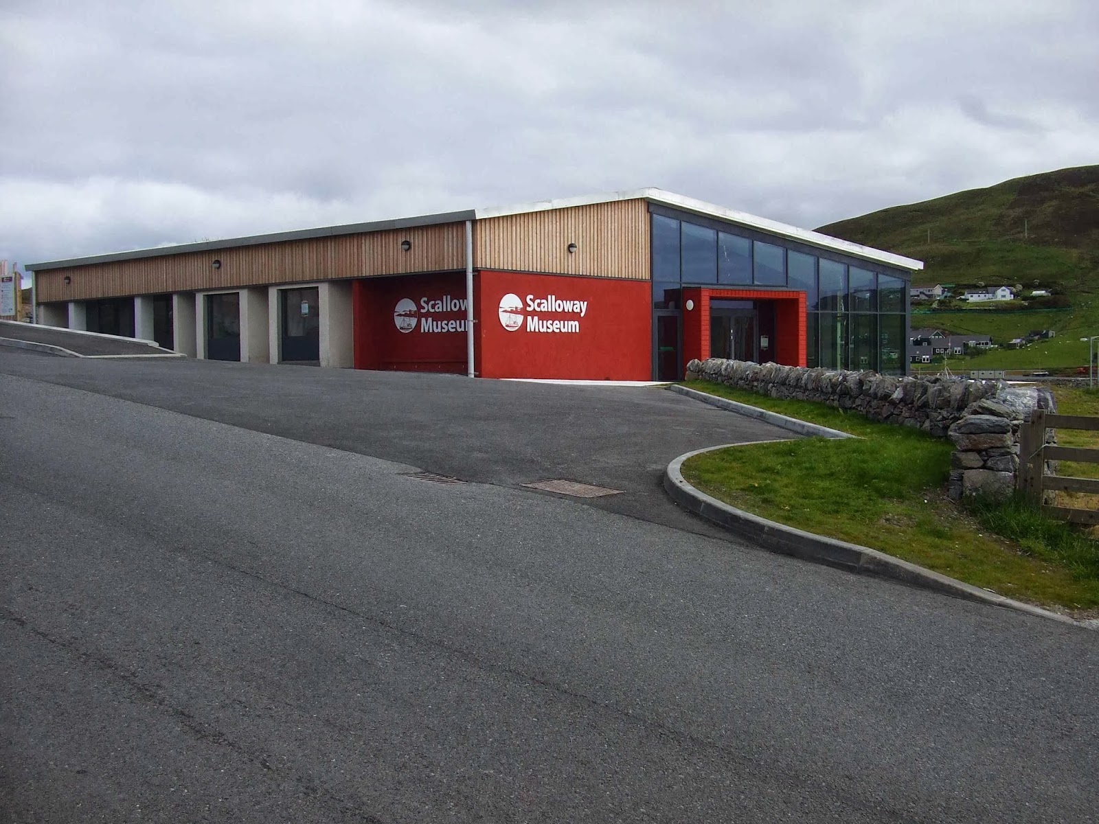 The Scalloway Museum, a long wood-clad building with a red entrance, on a bright day.