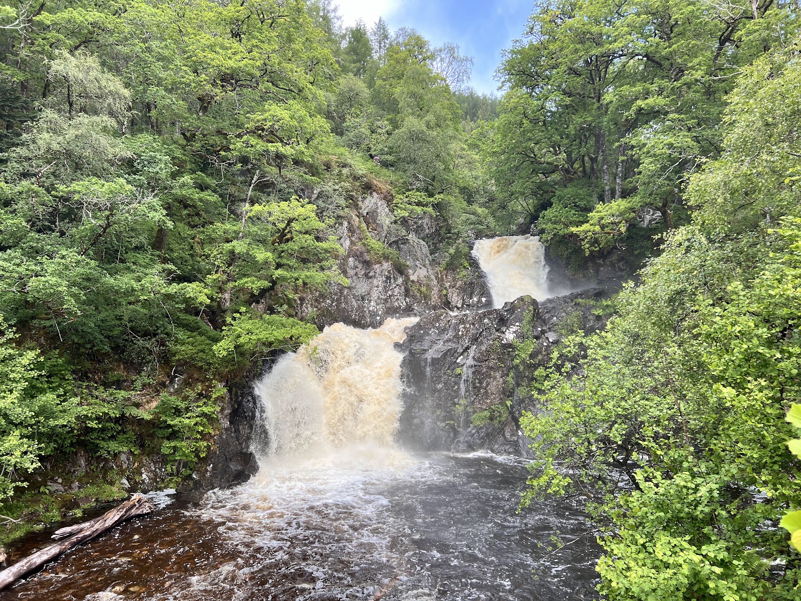 The Eas Chia-aig falls, two cascades of peaty water pouring over dark rock into a pool among green woods.