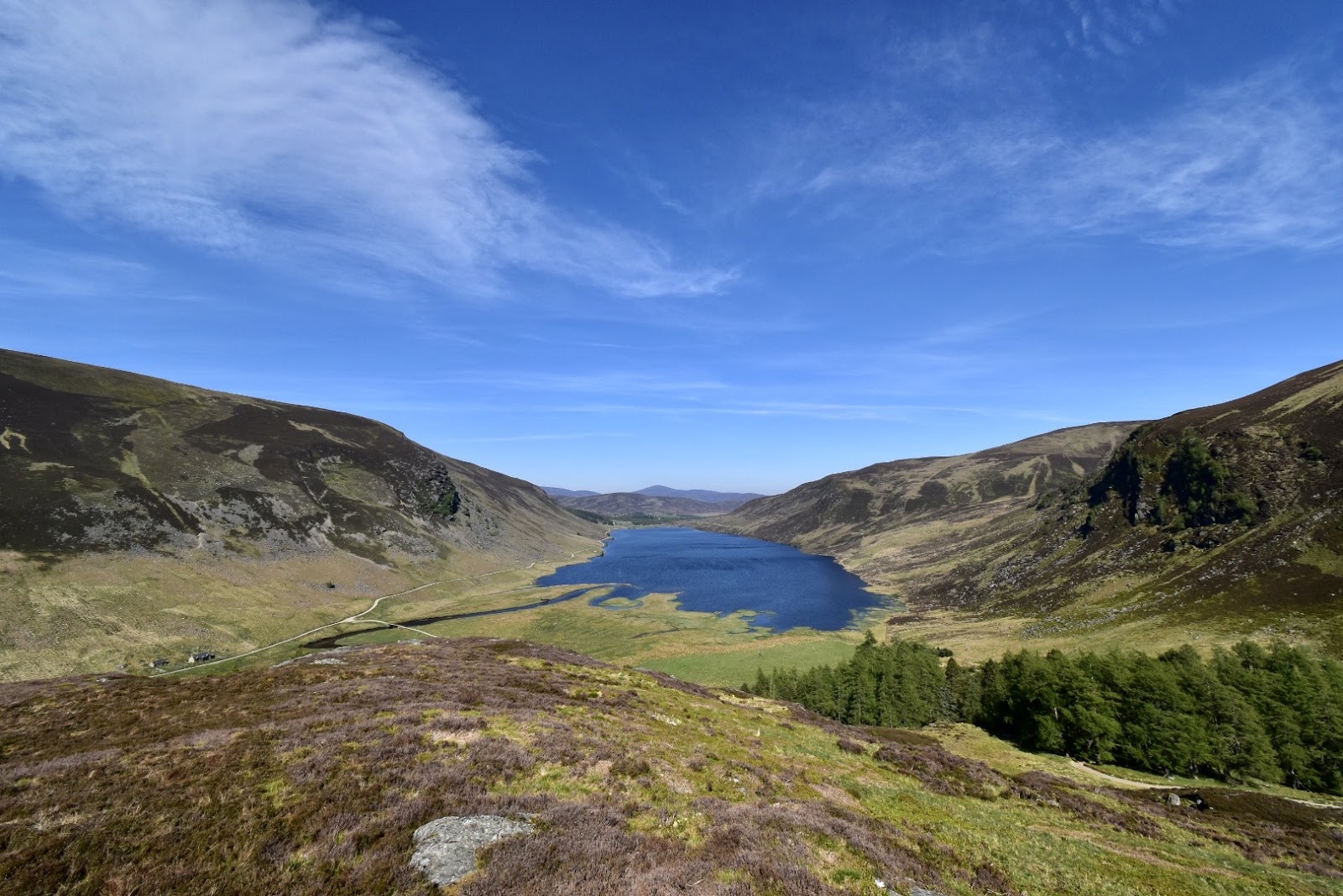 Loch Lee lying between steep hills at the head of Glen Esk, under a blue sky.