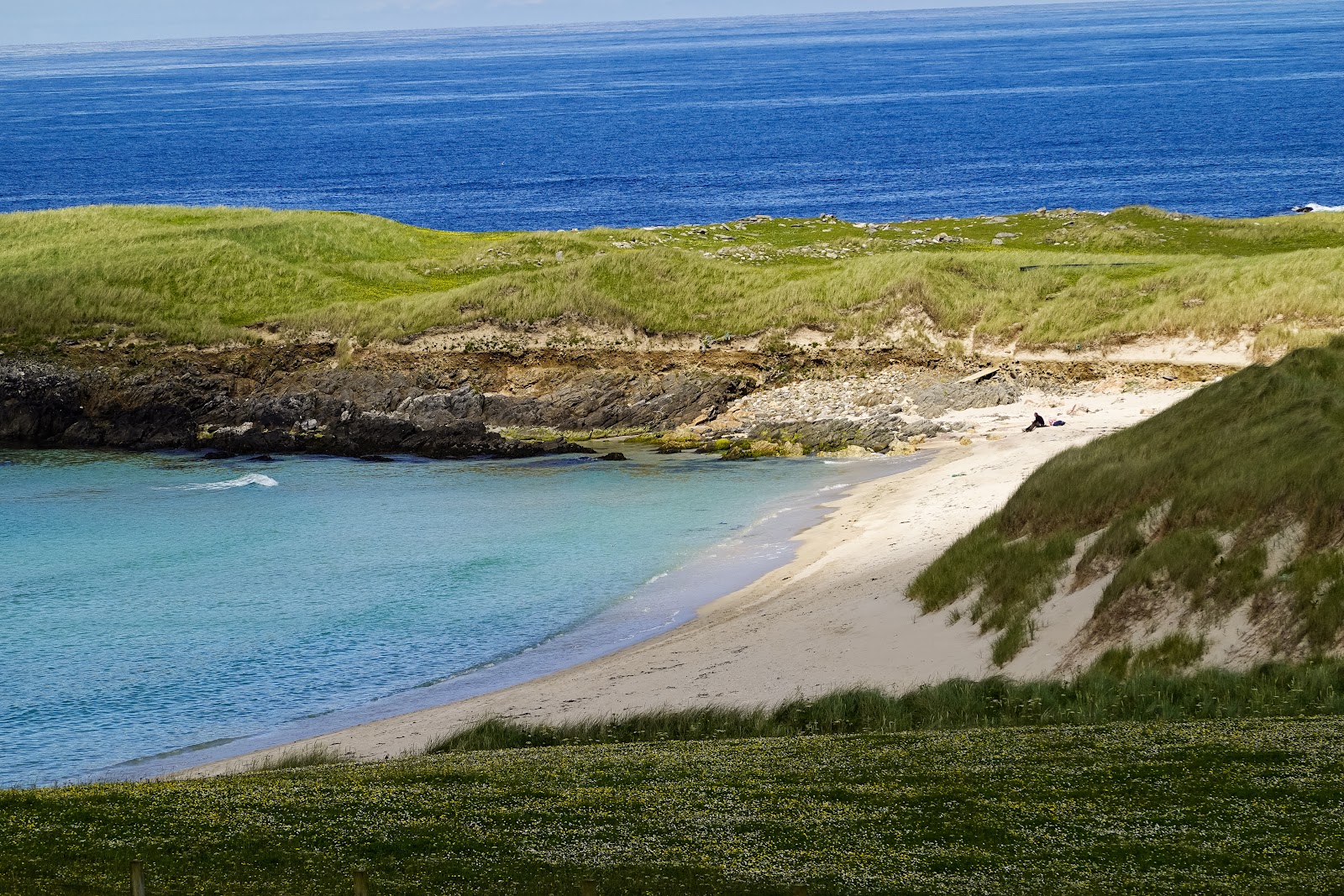 A sandy cove at Breckon below green dunes, the sea deep blue beyond.