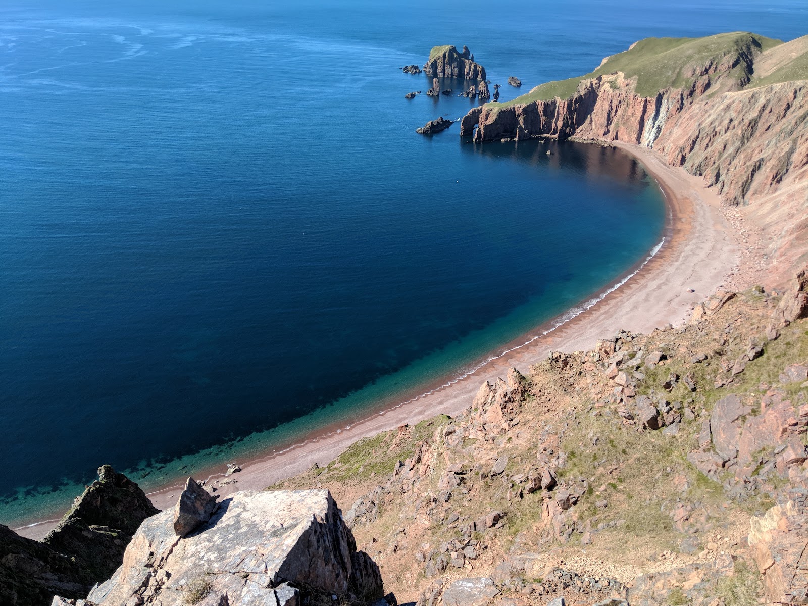 Da Lang Ayre, a curve of red shingle below steep granite cliffs, from above.